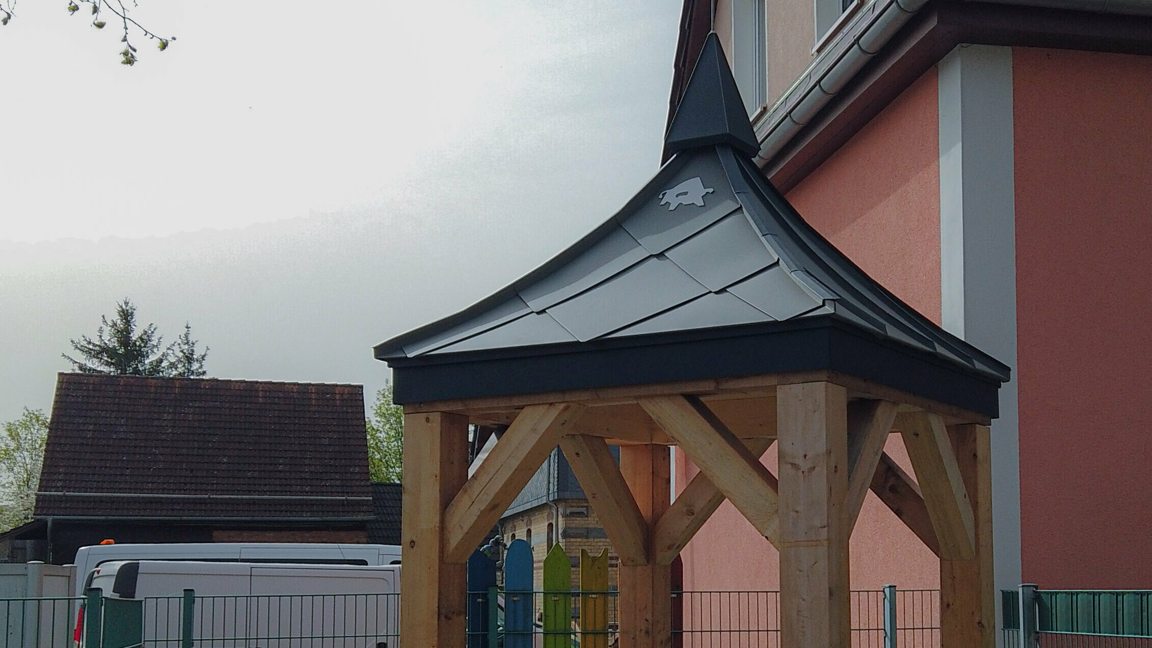 Unterstand mit PREFA Dachmodell und vier stabilen Holzbanken im Hof der Kindertagesstätte Regenbogen in Wernshausen.