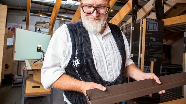 PREFA Techniker Tom Weiß mit einem Sockelprofil in Braun für die Siding Fassadenverlegung.