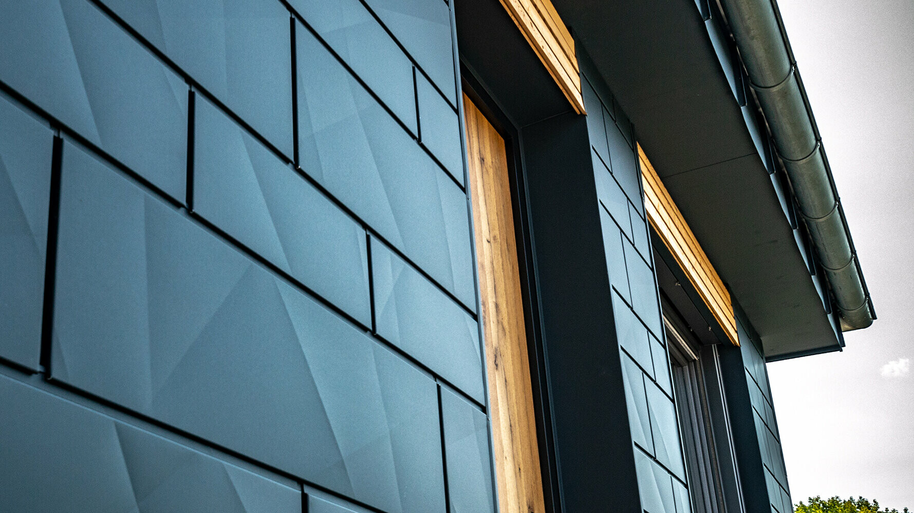 PREFA Fassadenpaneele mit geknickter Optik; PREFA Aluminium Siding.X in Anthrazit mit Holzfassade kombiniert.