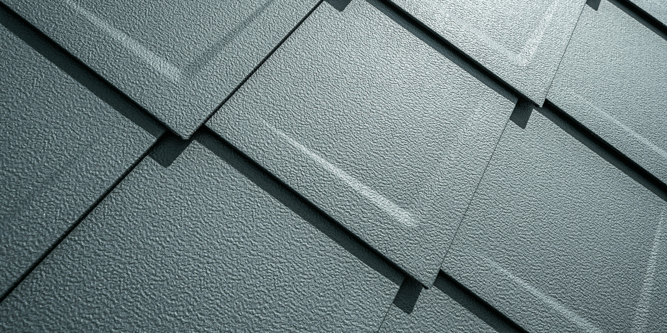 Detailaufnahme der PREFA Dachrauten 29 × 29 in der Farbe P.10 Anthrazit auf einem Einfamilienhaus nahe Düsseldorf. Auf dem Bild ist Stucco-Prägung, die durch Prägewalzen entsteht, genau zu erkennen. Durch dieses spezielle Verfahren wird das Aluminium unempfindlicher gegen Bearbeitungsspuren und somit verlegefreundlicher.