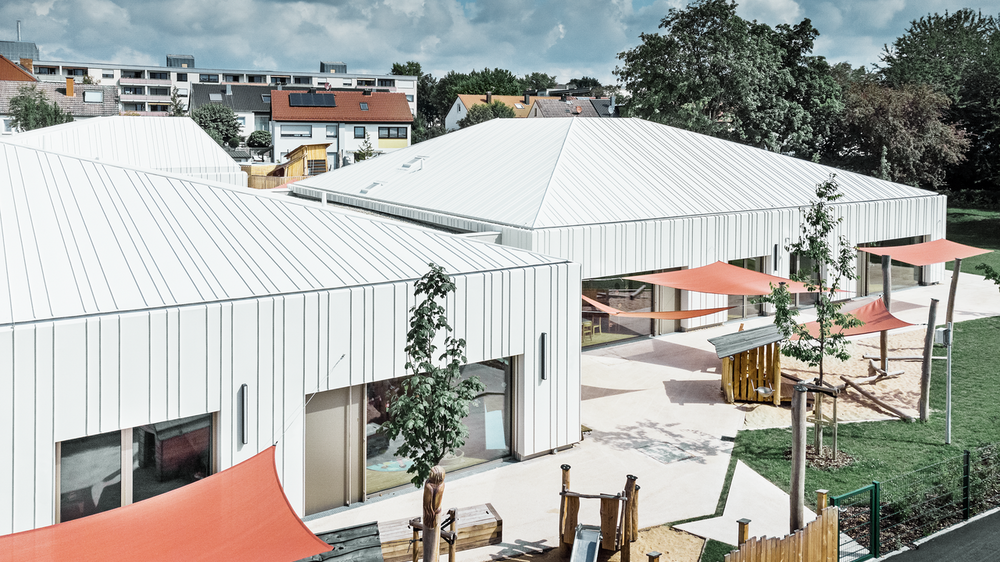 Zu sehen ist hier der Kindergarten in Niederwerrn, eingedeckt mit dem Prefalz Dachsystem von PREFA, mit Ansicht in den Garten.