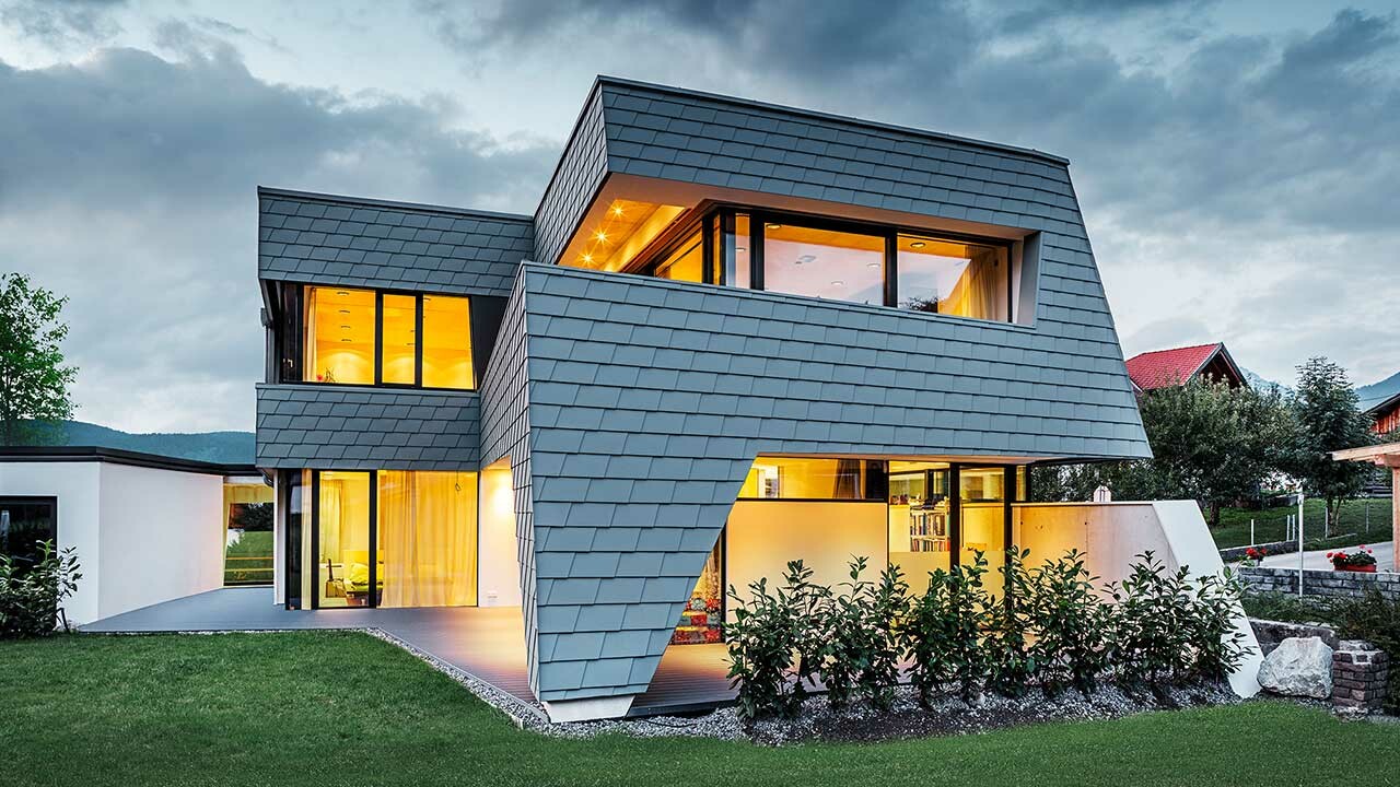 Aufnahme eines modernen Einfamilienhauses bei Abenddämmerung; Die Fassade ist mit der Wandschindel in Grau. 