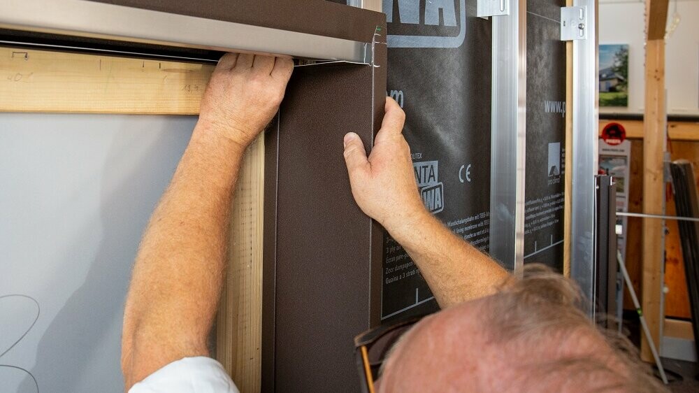 Nahaufnahme eines Fensters, bei dem die seitliche Laibung durch einen PREFA Techniker eingepasst wird.