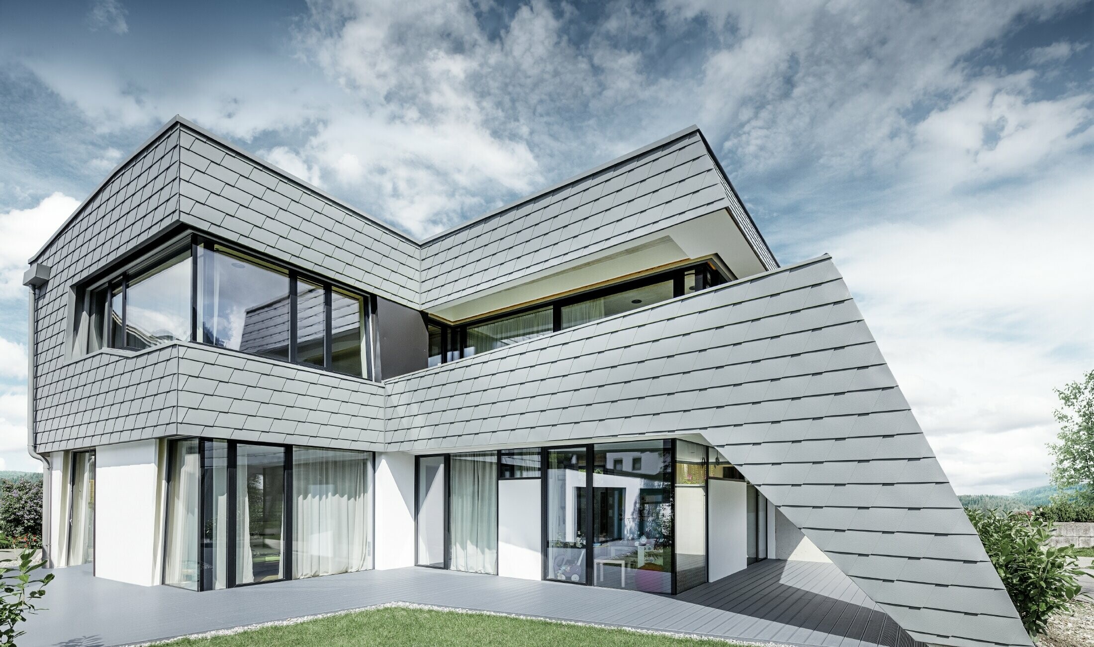 Modernes Einfamilienhaus mit Flachdach, großen Fensterflächen und einer Schindel-Fassade in hellgrau aus Aluminium von PREFA