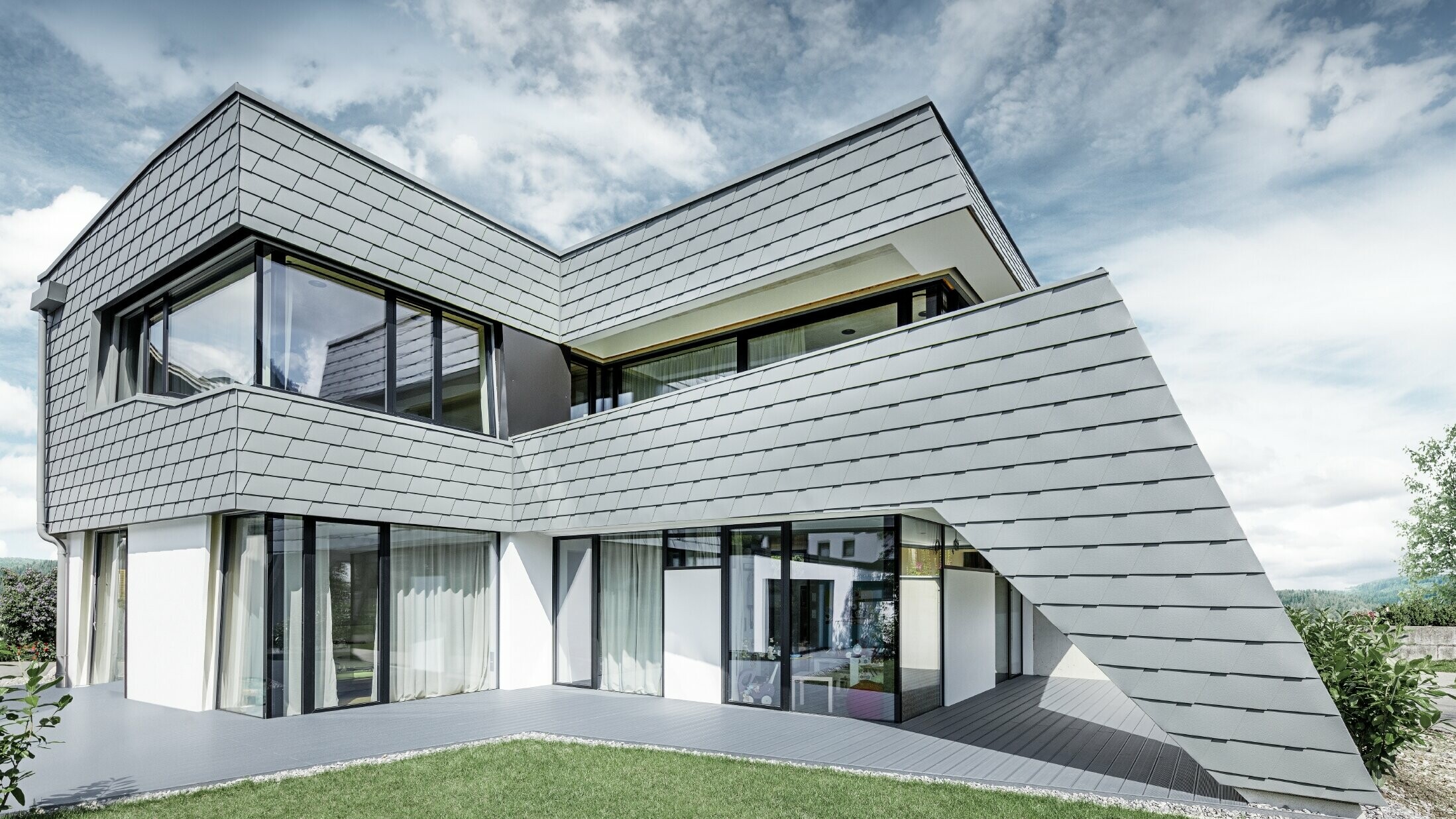 Modernes Einfamilienhaus mit Flachdach, großen Fensterflächen und einer Schindel-Fassade in hellgrau aus Aluminium von PREFA