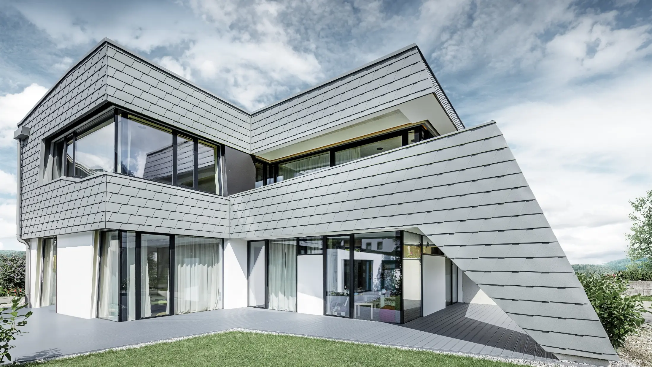 Modernes Einfamilienhaus mit Flachdach, großen Fensterflächen und einer Schindel-Fassade in hellgrau aus Aluminium von PREFA