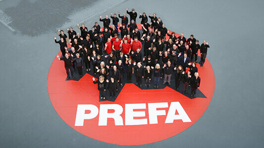 PREFA Team stehend auf einem roten PREFA Logo