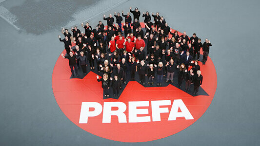 PREFA Team stehend auf einem roten PREFA Logo