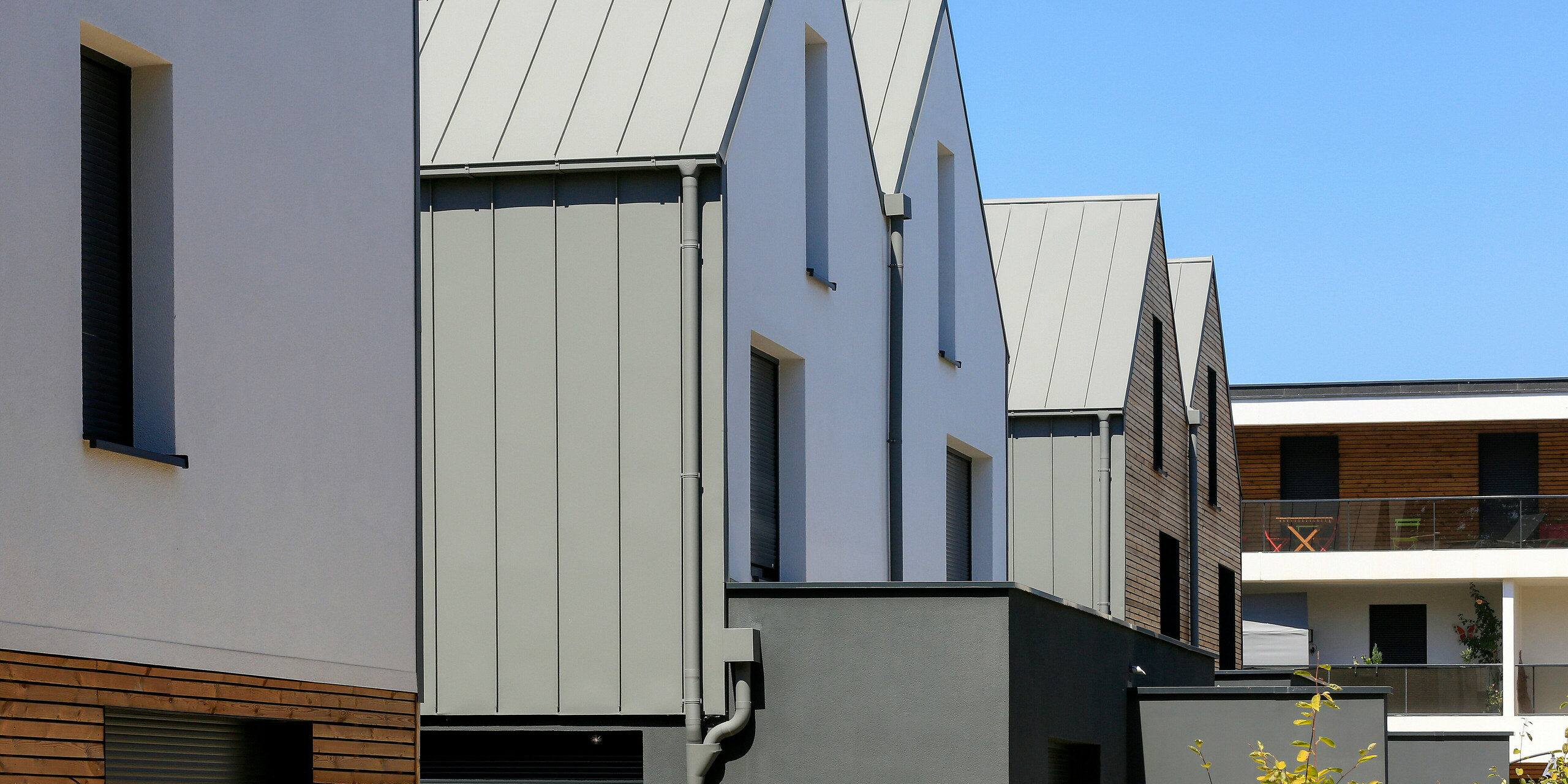 PREFALZ in Hellgrau zieht sich über die Fassaden und Satteldächer einer Reihenhaus-Siedlung in Mundolsheim. Die einheitlichen Gebäudehüllen aus Aluminium schaffen ein harmonisches Gesamtbild.