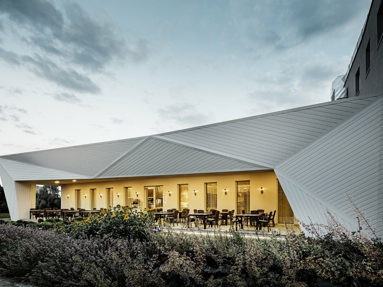 Frontansicht des modernen Restaurants Mimama in Budapest; eingedeckt mit PREFA Siding in P.10 Prefaweiß; umgeben von idyllischer Natur und einem See