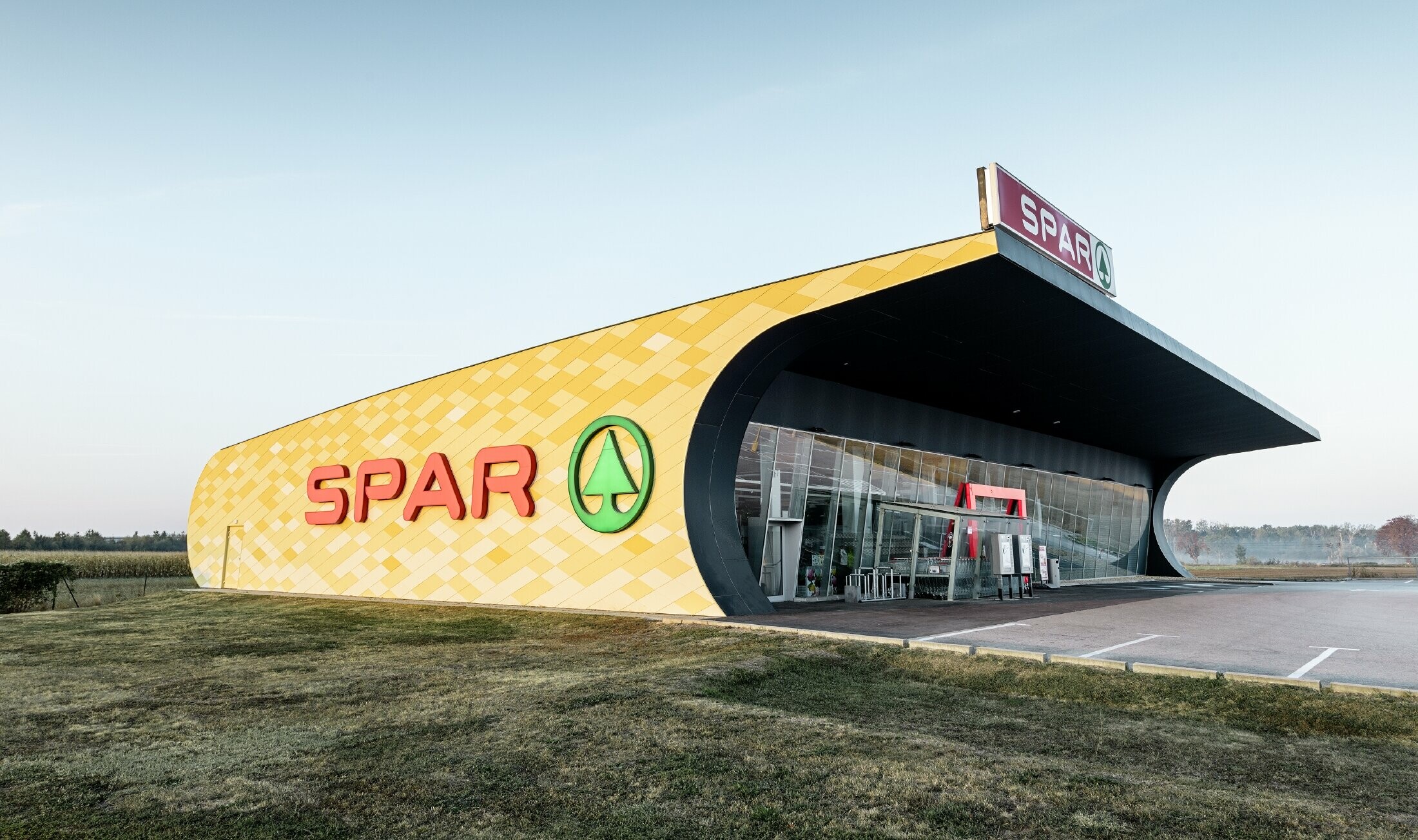 Spar Filiale mit einer Aluminiumfassade in gelb-orangen Karos und Spar Logo