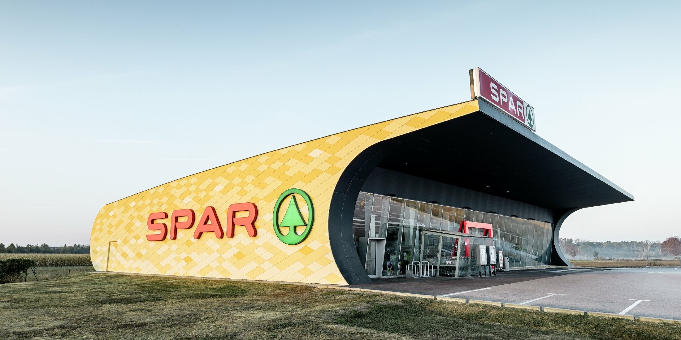 Spar Filiale mit einer Aluminiumfassade in gelb-orangen Karos und Spar Logo