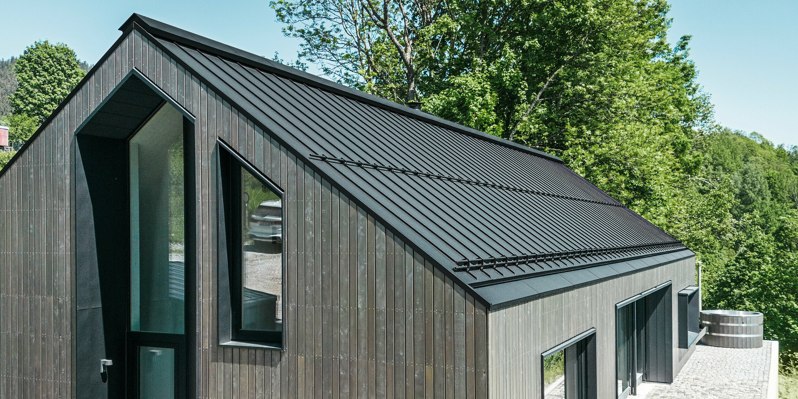 Hochformatbild von luxuriösem Holzmassivhaus in Kuncice, CZ. Das Einfamilienhaus mit den großen Fenstern verfügt über ein PREFALZ-Dach aus Aluminium in Schwarz.