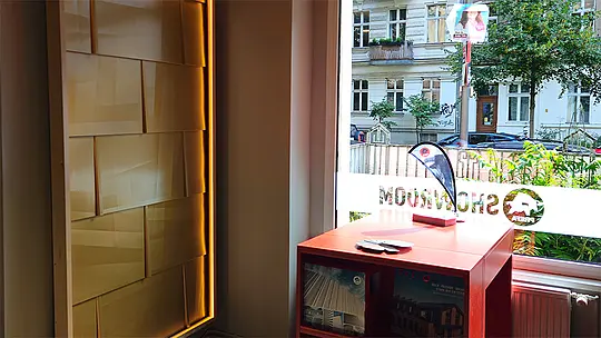 Produktpräsentation im PREFA Showroom Berlin mit beleuchteter Fassadenmusterwand und Informationsmaterial am Schaufenster.