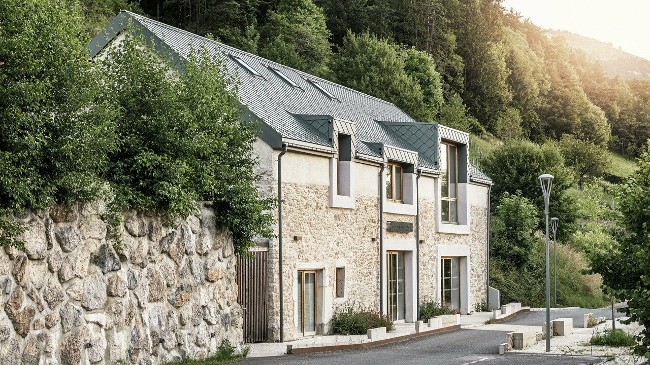 Seitenansicht der restaurierten Scheune „La Grange à Gaby“ in Engins, Frankreich. Das Gebäude vereint traditionelles Steinmauerwerk mit einem modernen PREFA-Aluminiumdach aus 29 × 29 cm großen Rauten. Die sorgfältige Sanierung verbindet historische Bauweisen mit langlebigen Materialien.