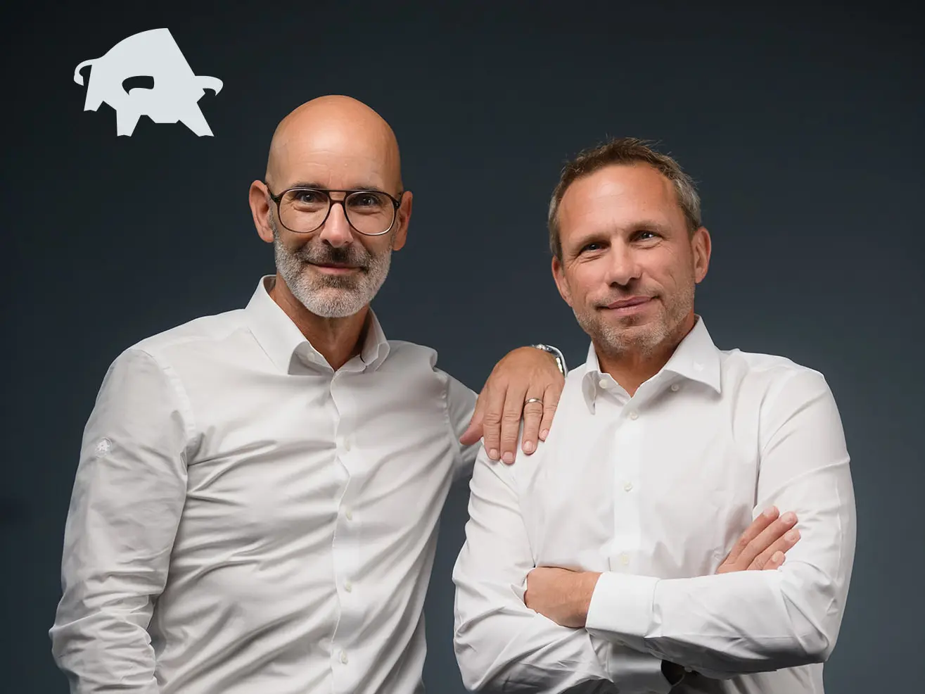 Die Leiter der Vertriebsgebiete Süd, Frieder Zaiß (Süd-Ost) und Markus Sack (Süd-West) nebeneinander vor grauem Hintergrund. In der linken oberen Ecke ist der PREFA Stier abgebildet.