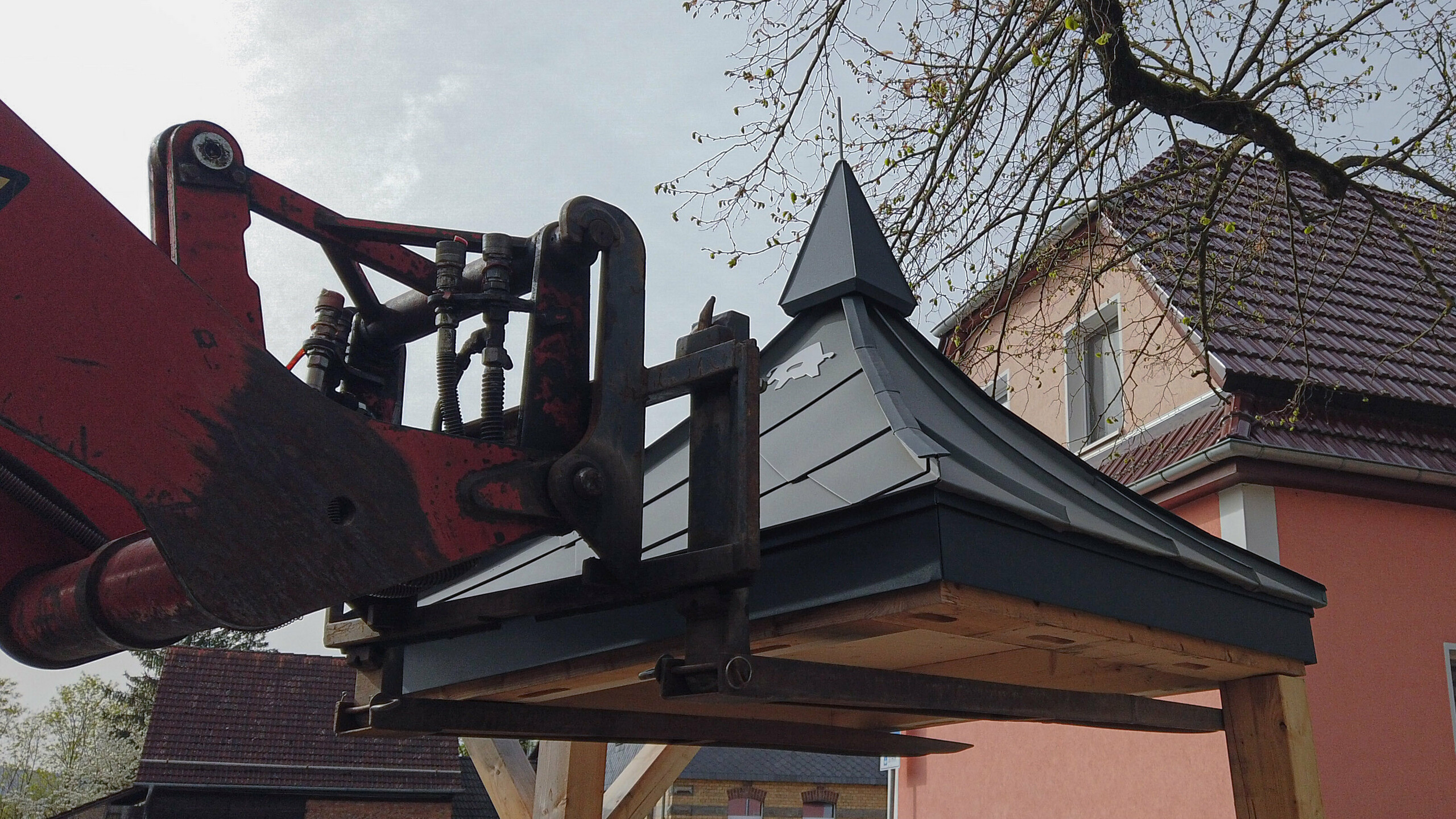 Ein kleines PREFA-Dach wird mittels Gabelstapler auf Holzbalken gesetzt.
