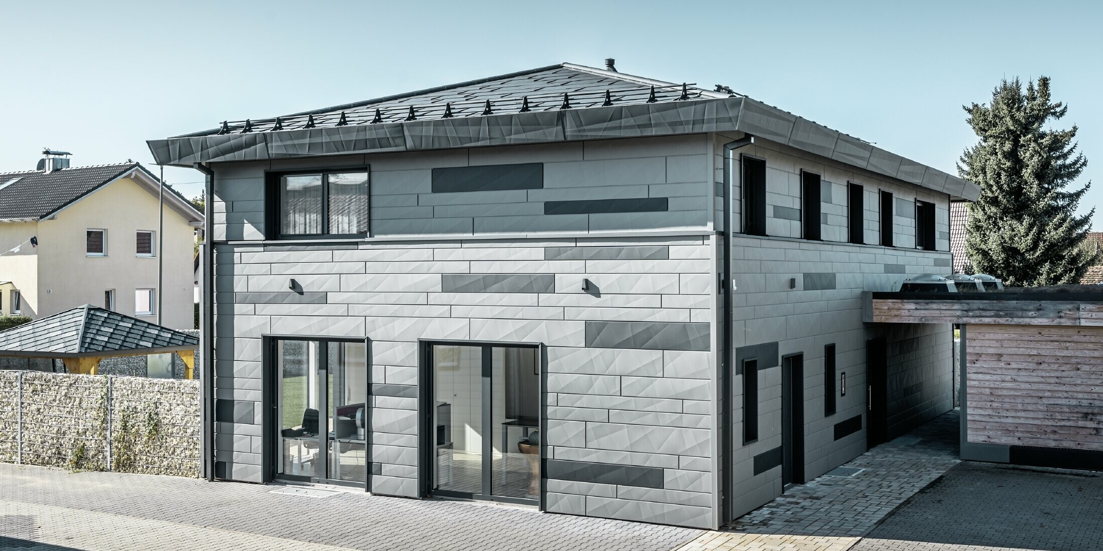 Blick von der Straße auf ein Einfamilienhaus in Türksheim. Die zweifarbige Fassade und die Kanten der FX.12-Paneele verleihen dem Haus ein modernes Aussehen.