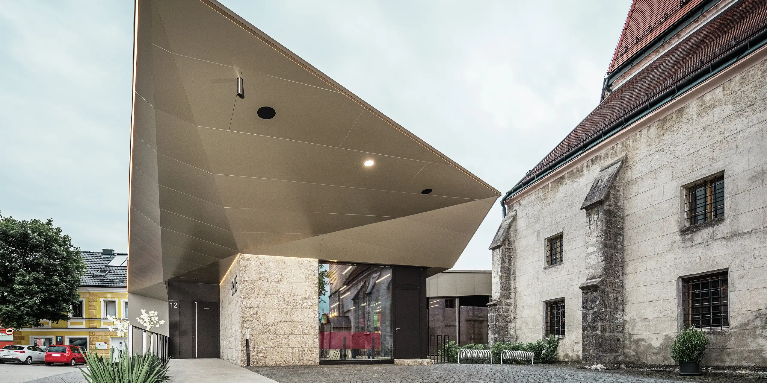 Ein Blick unter das kantig gefaltete Vordach offenbart die raffinierte Verarbeitung der bronzefarbenen PREFA Aluminium Verbundplatten. Diese bieten optimalen Korrosionsschutz, sind UV-beständig und verleihen der Konstruktion eine futuristische, fast schwerelose Ästhetik.
