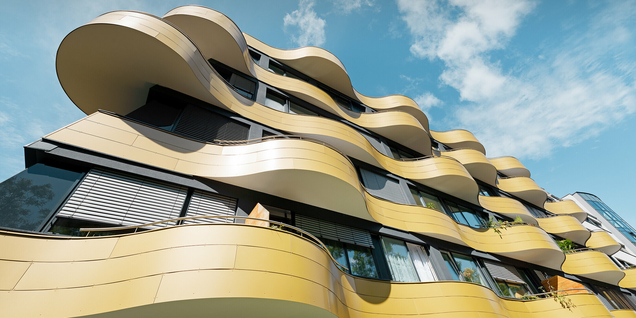 Froschperspektive auf die einzigartige Fassadengestaltung der Wohnhausanlage "Goldene Welle" in Graz. Die goldenen Balkone mit ihren speziellen Rundungen wurden mit Aluminium Verbundplatten bekleidet.