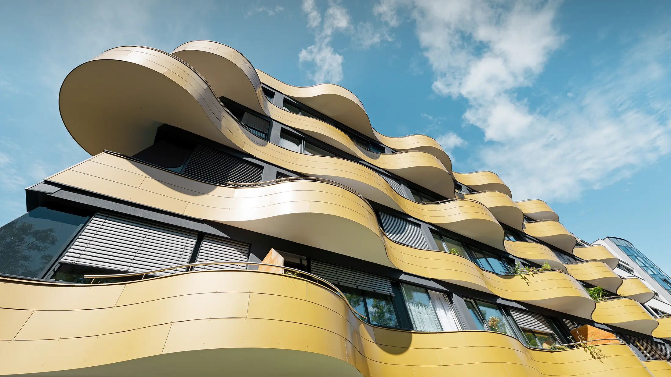 Froschperspektive auf die einzigartige Fassadengestaltung der Wohnhausanlage "Goldene Welle" in Graz. Die goldenen Balkone mit ihren speziellen Rundungen wurden mit Aluminium Verbundplatten bekleidet.