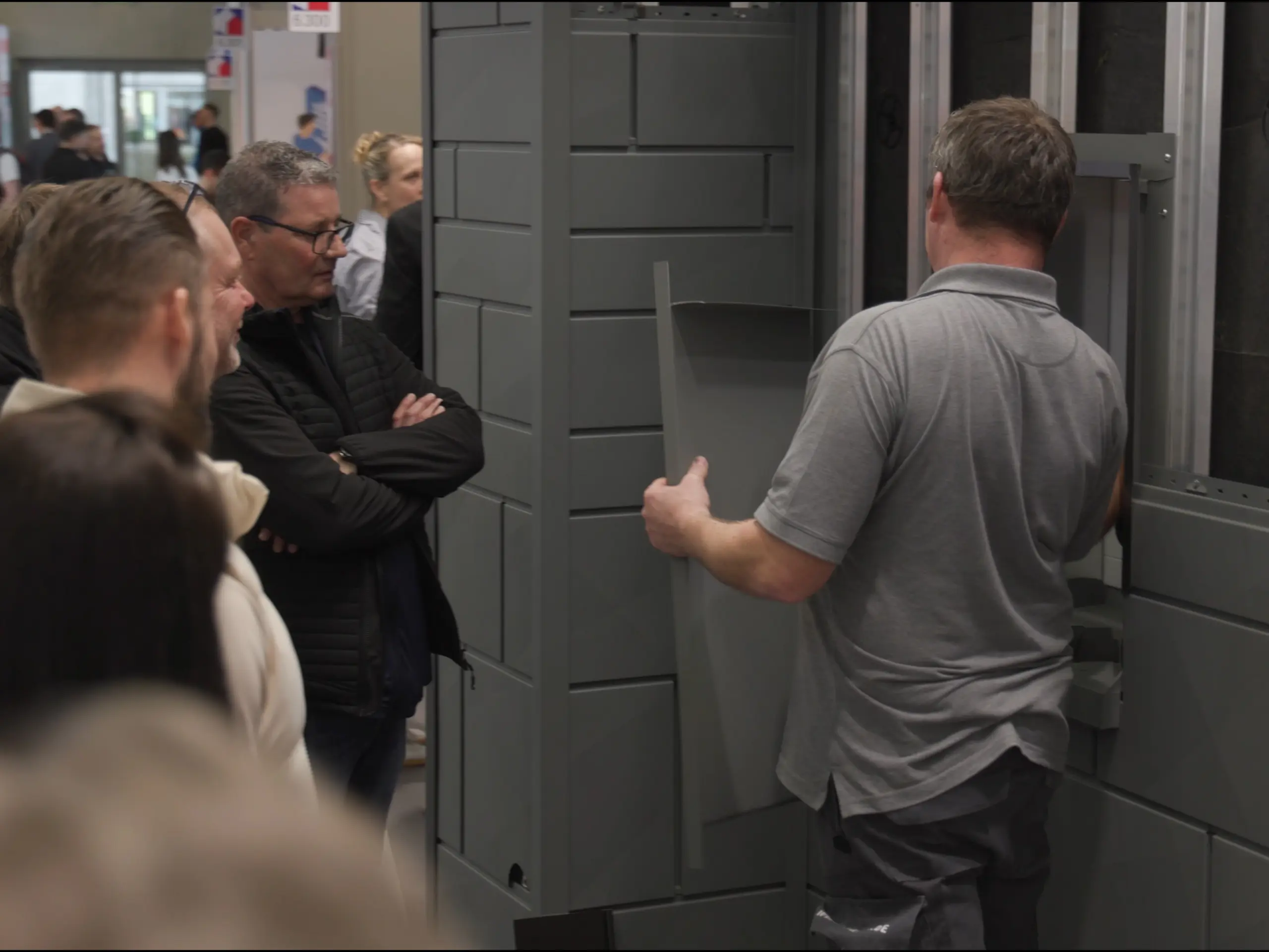 PREFA Trainer Ralf Naumer erklärt interessierten Messebesuchern den Aufbau der vorgehängt hinterlüfteten PREFA Fassade am PREFA Academy Messestand auf der Dach+Holz Messe 2026 in Köln.