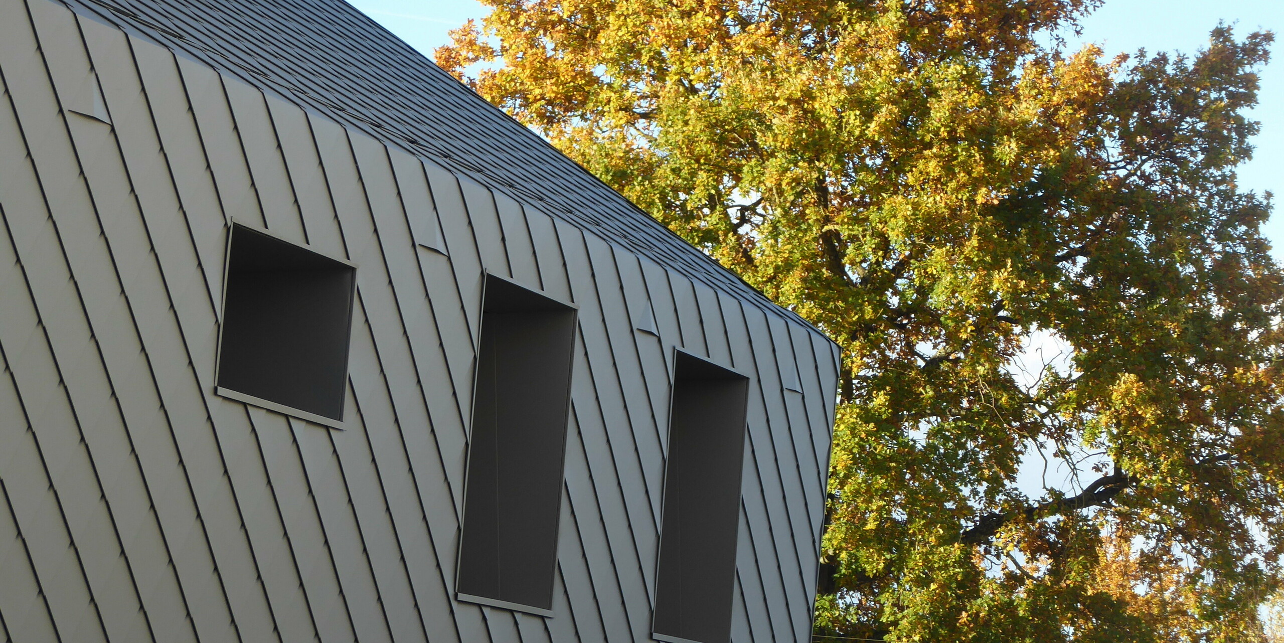 Nahaufnahme des Übergangs vom Dach zur Fassade mit PREFA Rauten aus Aluminium auf Einfamilienhaus in Acigne