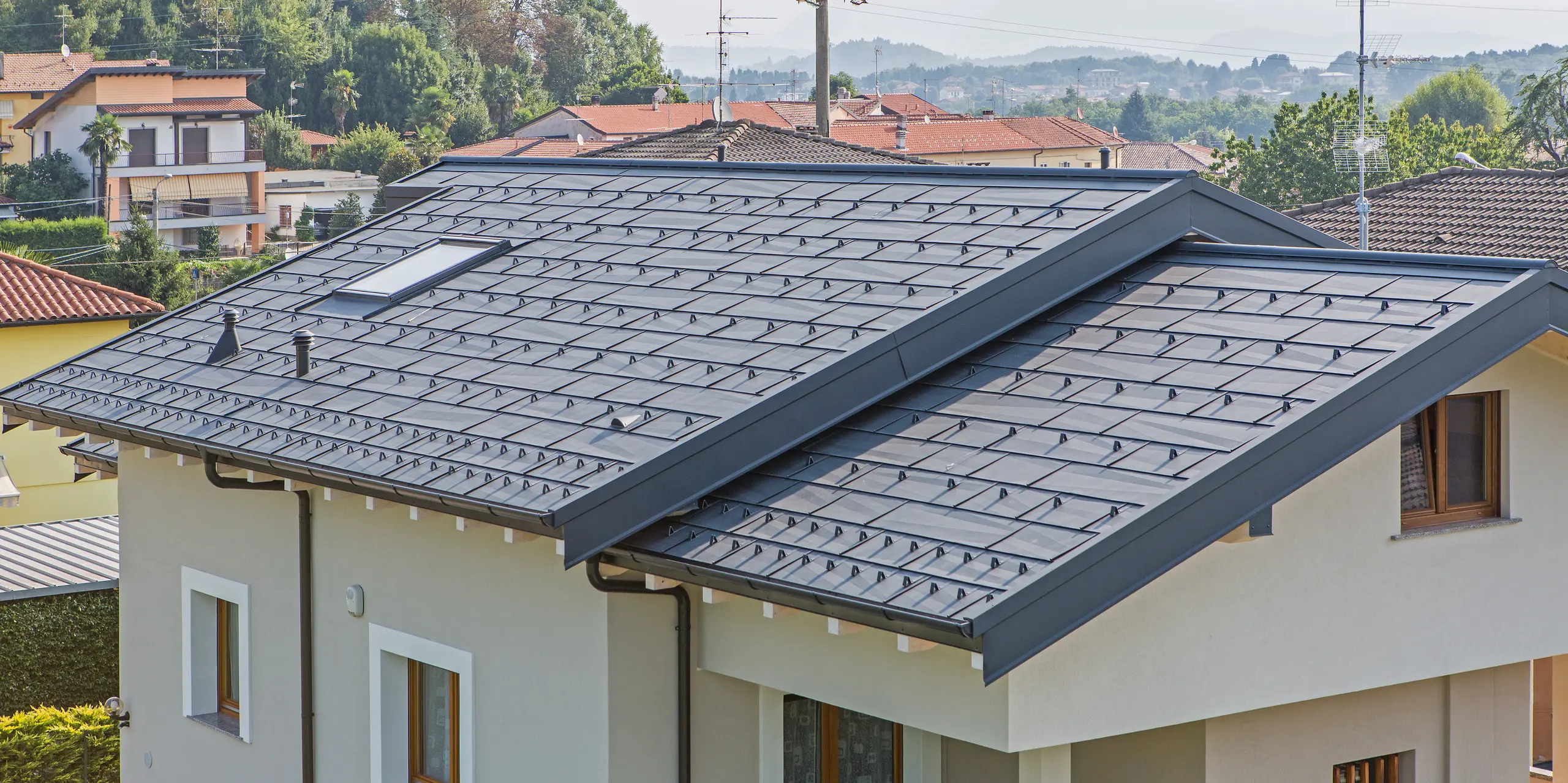 Detailaufnahme des PREFA Dachs FX.12 in P.10 Anthrazit auf einem Einfamilienhaus in Beregazzo, Italien. Die markanten, unregelmäßig gekanteten Aluminium-Dachpaneele erzeugen ein faszinierendes geometrisches Muster und ein dynamisches Lichtspiel. Die elegante Dachfläche vereint moderne Architektur mit den Vorteilen von PREFA Aluminium: langlebig, witterungsbeständig und optisch außergewöhnlich.