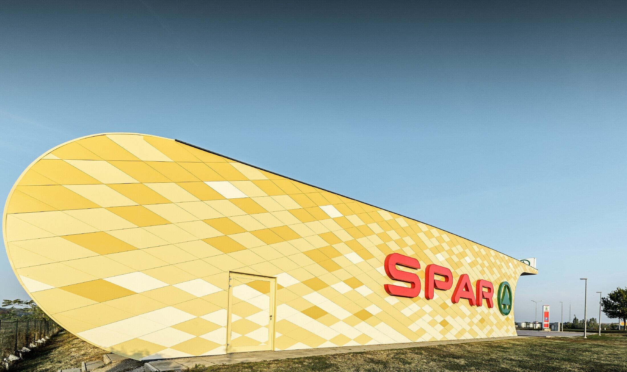 Spar Filiale mit einer Aluminiumfassade in gelb-orangen Karos und Spar Logo