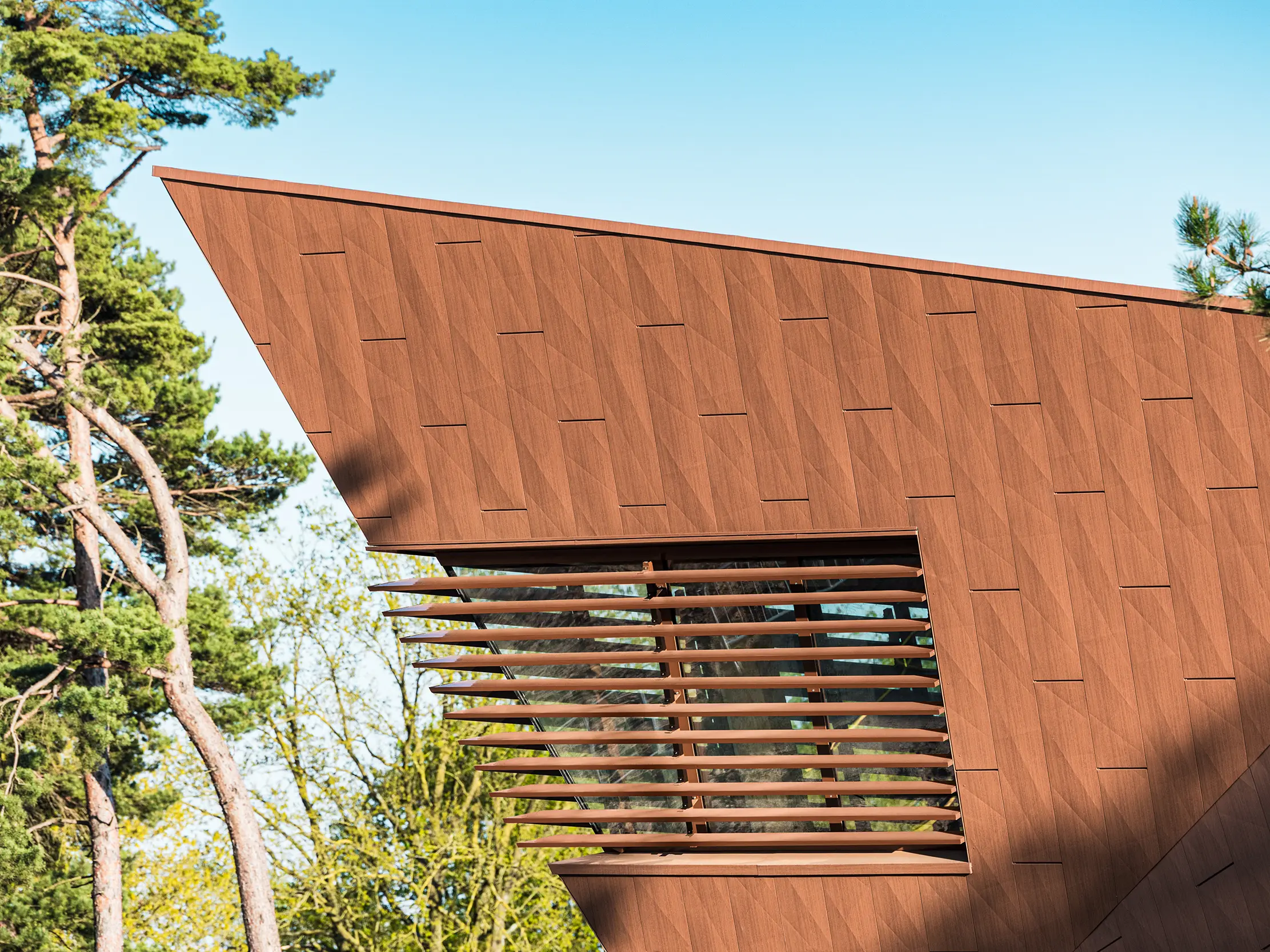 Das Trinkwasserpumpwerk in Lottum (Niederlande) fügt sich als skulpturales Bauvolumen harmonisch in die naturnahe Umgebung ein. Die prägnante PREFA Siding.X-Aluminiumfassade in warmer Rostoptik bildet einen spannenden Kontrast zu der grünen Wiese und den Hügeln und fasziniert mit ihrer fein strukturierten, lebendigen Oberfläche. Schlanke, vertikale Öffnungen setzen präzise Akzente. Die langlebigen, leichten und vollständig recycelbaren PREFA-Aluminium-Paneele überzeugen durch hohe Witterungsbeständigkeit, Farbkonstanz und eine nachhaltige, wartungsarme Gebäudehülle. Damit ist das Trinkwasserpumpwerk ein architektonischer Eyecatcher im Infrastrukturbau.
