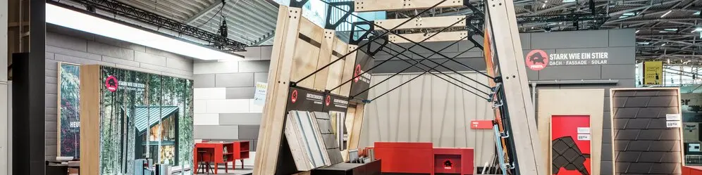 Moderner PREFA Messestand mit offener Konstruktion und einer Auswahl an Dach- und Fassadensystemen aus Aluminium. Musterflächen und Produktdisplays zeigen innovative Lösungen für Dach, Fassade, Solar. und Hochwasserschutz.