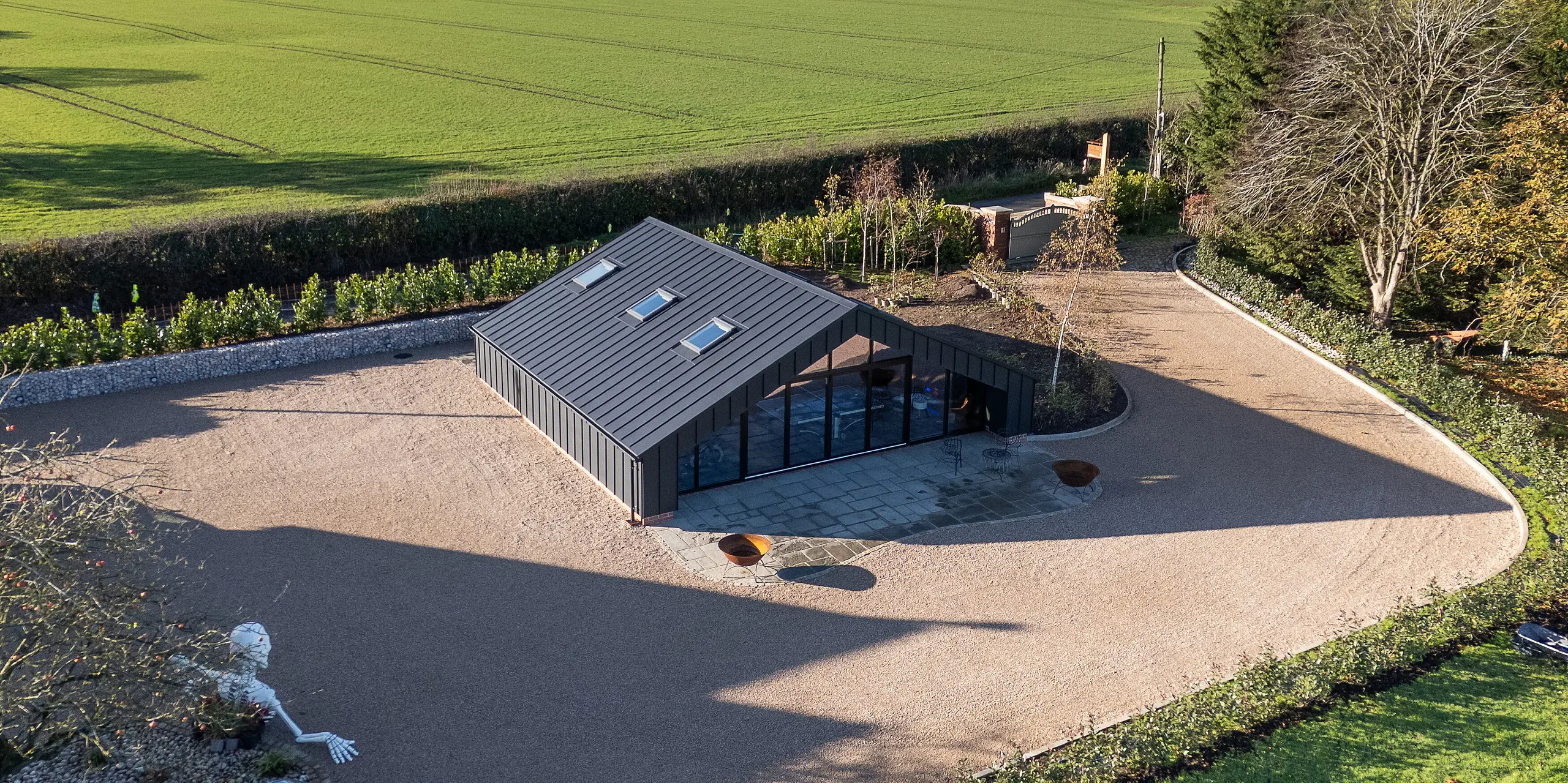 Weitläufige Vogelperspektive auf das moderne Freizeitgebäude mit vollständig verkleideter PREFA Aluminiumfassade und PREFALZ Dachflächen in P.10 Schwarz. Die präzisen Stehfalzlinien, die markante Dachgeometrie und die großflächige Glasfront setzen starke architektonische Akzente. Die robuste, witterungsbeständige Aluminiumhülle fügt sich harmonisch in die offene Landschaft ein.