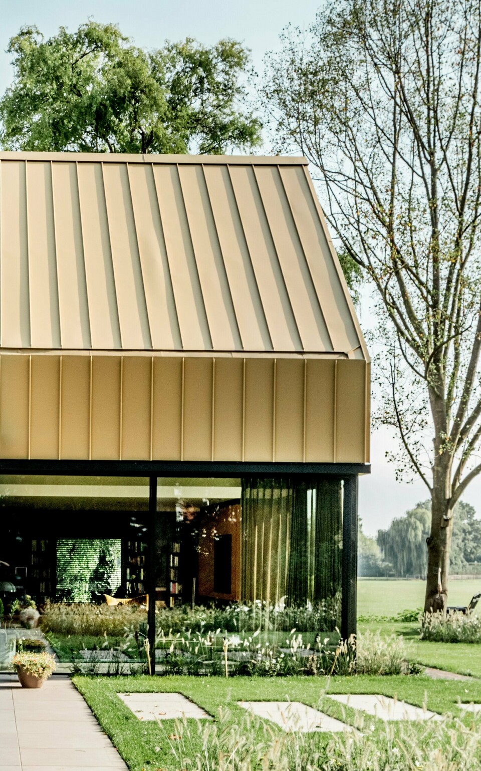 Moderne Architektur mit goldfarbenem PREFA Band- und Blechmaterial, das sowohl die Fassadenverkleidung als auch das Dach des Gebäudes prägt. Die präzise Verarbeitung und das hochwertige Design unterstreichen die vielseitigen Einsatzmöglichkeiten der PREFA Produkte für anspruchsvolle Architekturprojekte. Das Bild zeigt die perfekte Kombination aus Ästhetik und Funktionalität im "Goldenen Haus".