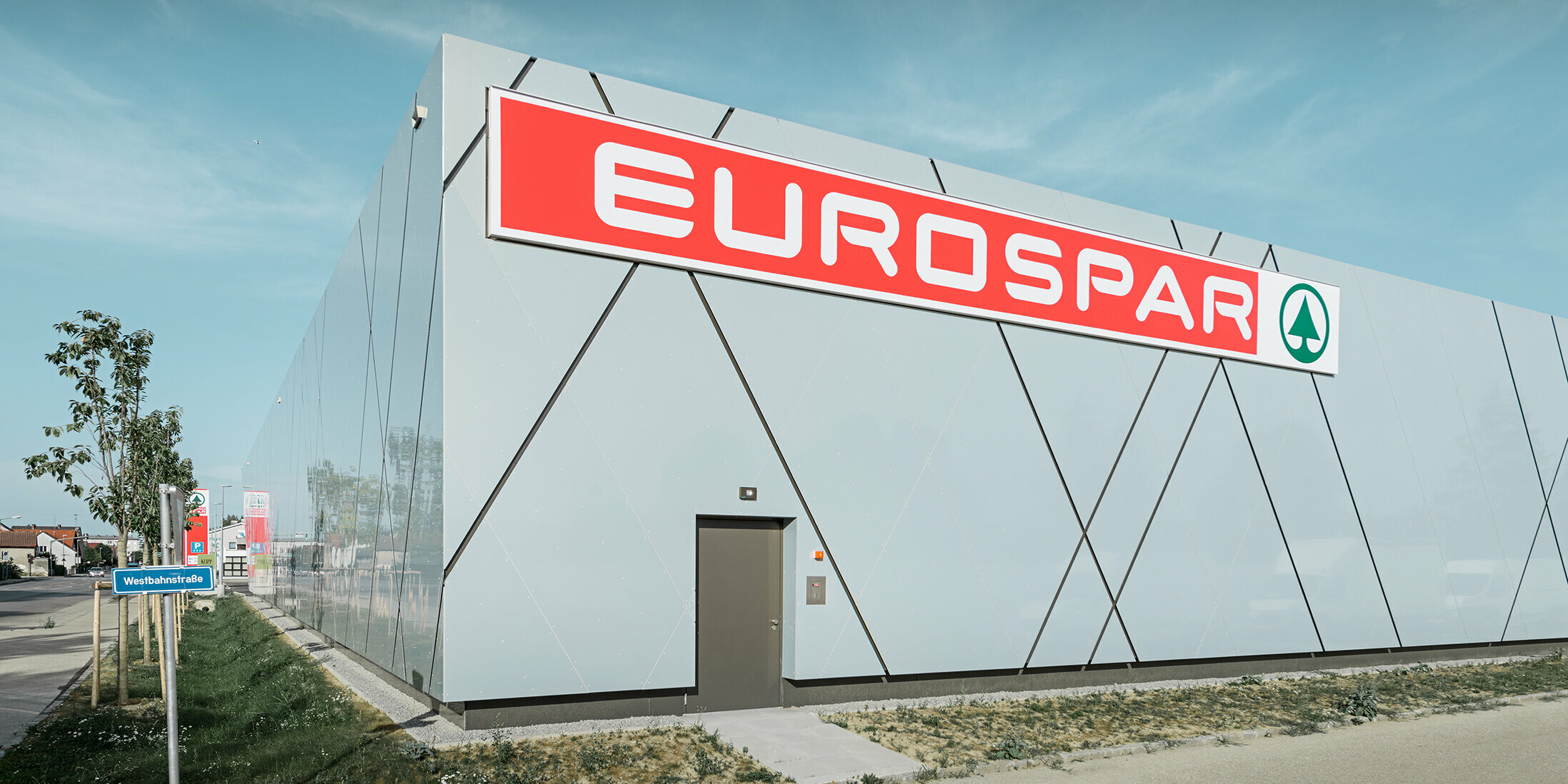 Die Rückseite des Gebäudes präsentiert das großflächige Eurospar-Logo auf einer glatten PREFA Aluminiumfassade. Die Sonderfarbe Silver Gold und die diagonalen Fugen setzen ein modernes Statement und machen die Filiale zum optischen Blickfang im Stadtbild von Wels.