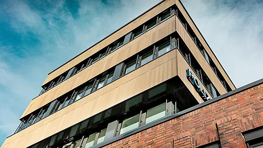 Dynamische Untersicht des Polizeikommissariats 43 in Hamburg: Der klar geschnittene Neubau beeindruckt mit einer PREFA Aluminiumfassade aus Strangpressprofilen „Zacke“ in elegantem Mittelbronze. Die fein gerippte Oberfläche wird zum visuellen Eyecatcher und erzeugt spannende Licht- und Schattenverläufe entlang der horizontalen Fensterbänder. Im Kontrast zum massiven Backstein entsteht ein kraftvolles Architekturstatement. PREFA Aluminium überzeugt dabei durch Korrosionsbeständigkeit, Langlebigkeit und geringen Wartungsaufwand – ideal für nachhaltige, präzise Fassadengestaltung.