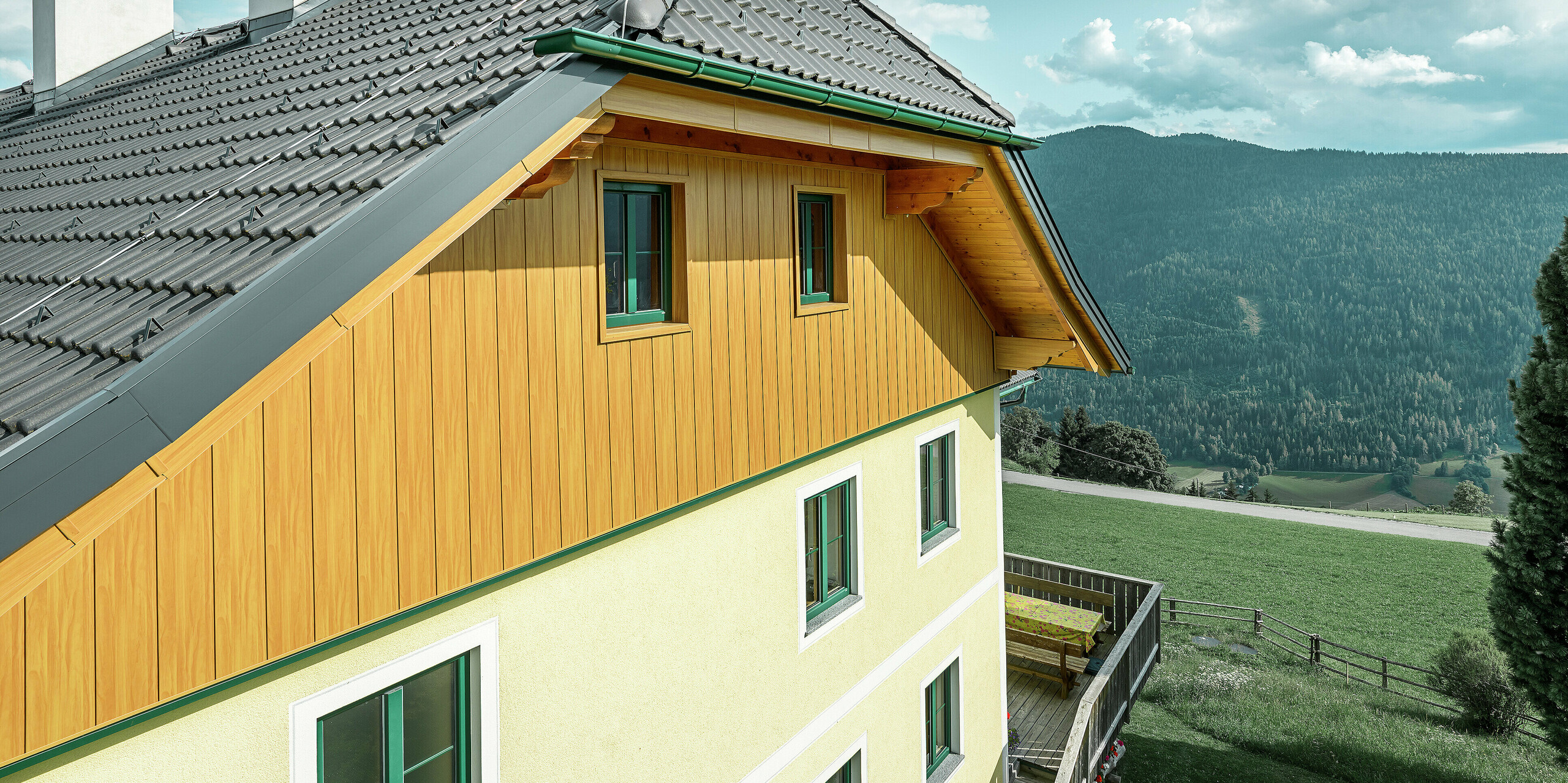Detailansicht der Giebelverkleidung mit PREFA Sidings in Eiche natur an einem Wohnhaus in Ranten mit Blick auf die umliegende Berglandschaft.