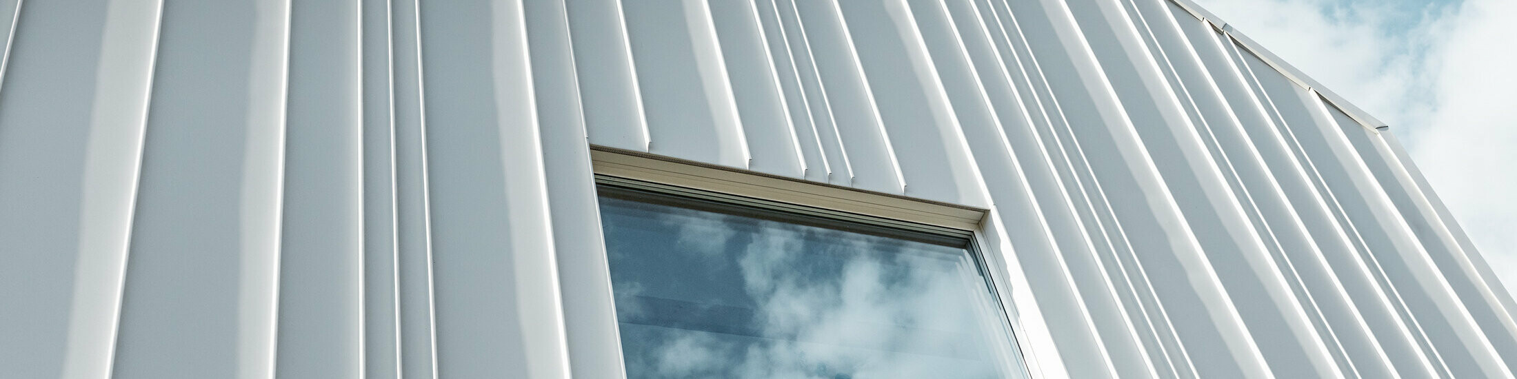 weißes PREFALZ als Winkelstehfalz an der Fassade mit unterschiedlichen Scharenbreiten und einem Fenster