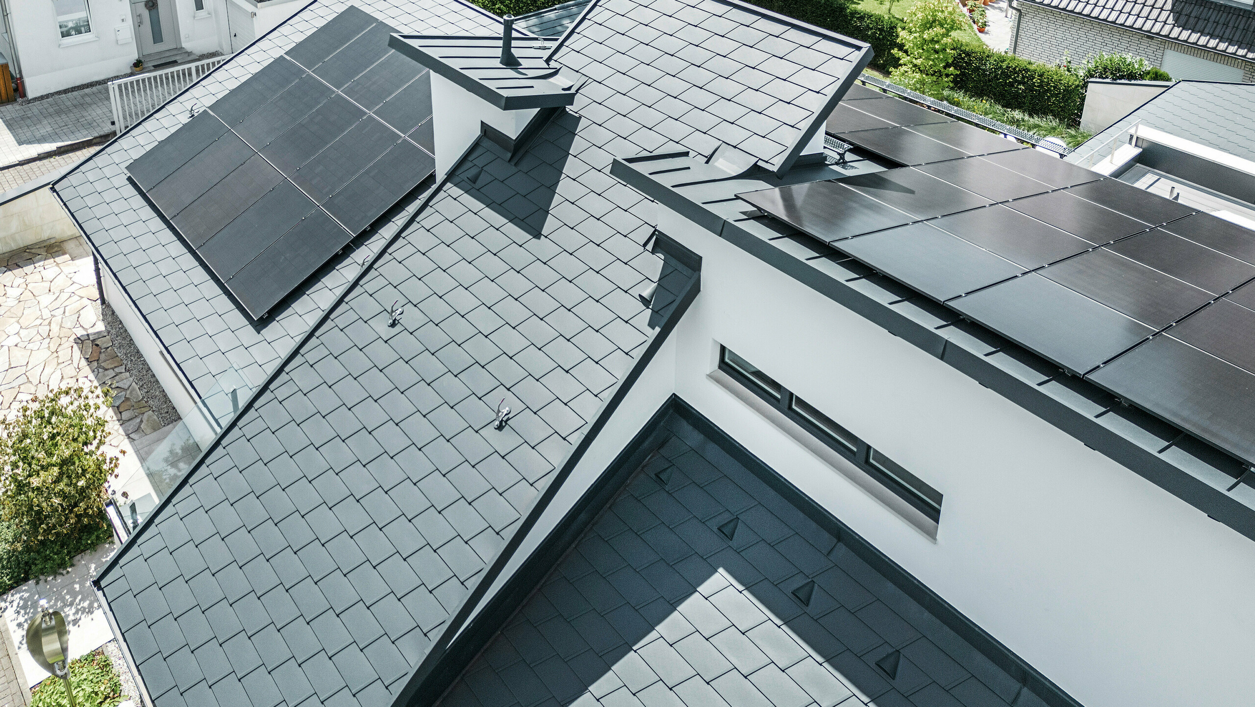 Modernes Einfamilienhaus in Dortmund mit einer fortschrittlichen Photovoltaikanlage, installiert auf einem PREFA Dachsystem bestehend aus Dachschindeln DS.19 und PREFALZ Stehfalzdeckung in der Farbe P.10 Anthrazit. Die PV-Anlage ist mittels Vario Solarhalter für die Dachschindeln und des PREFALZ Vario Solarhalter für die Stehfalzbahnen befestigt. Die Solaranlage gewährleistet eine effiziente Energieerzeugung aus erneuerbaren Energiequellen. Das durchdachte Dachdesign bietet eine optimale Balance zwischen Ästhetik und Funktionalität.