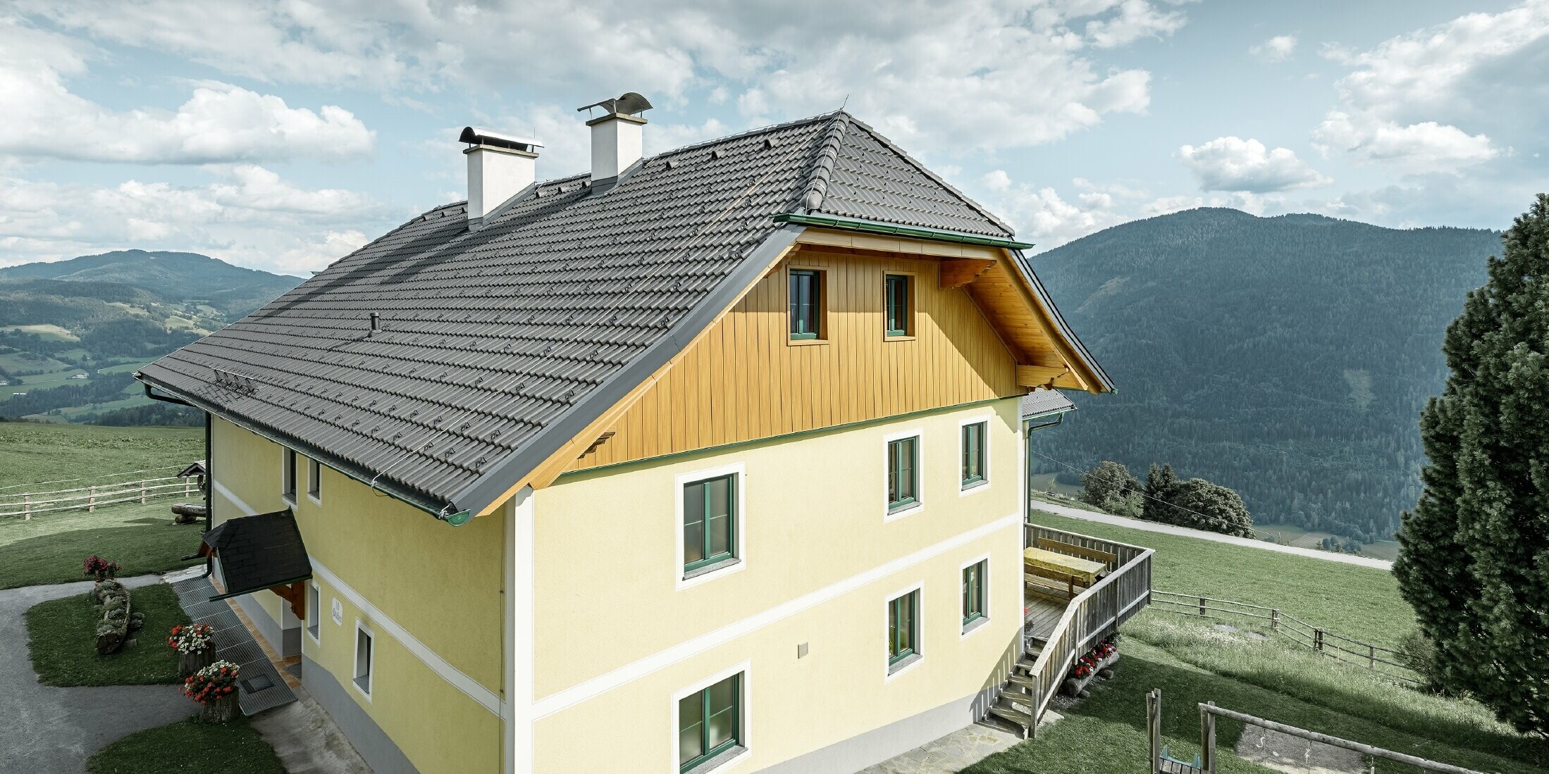 Giebelverkleidung aus witterungsbeständigem Aluminium: Ein mehrstöckiges Wohnhaus in Ranten wurde an der Giebelseite mit PREFA Sidings in Holzoptik verkleidet. Das traditionelle Wohnhaus liegt idyllisch mit Blick auf die Berge und einem kleinen Kinderspielplatz im Garten.