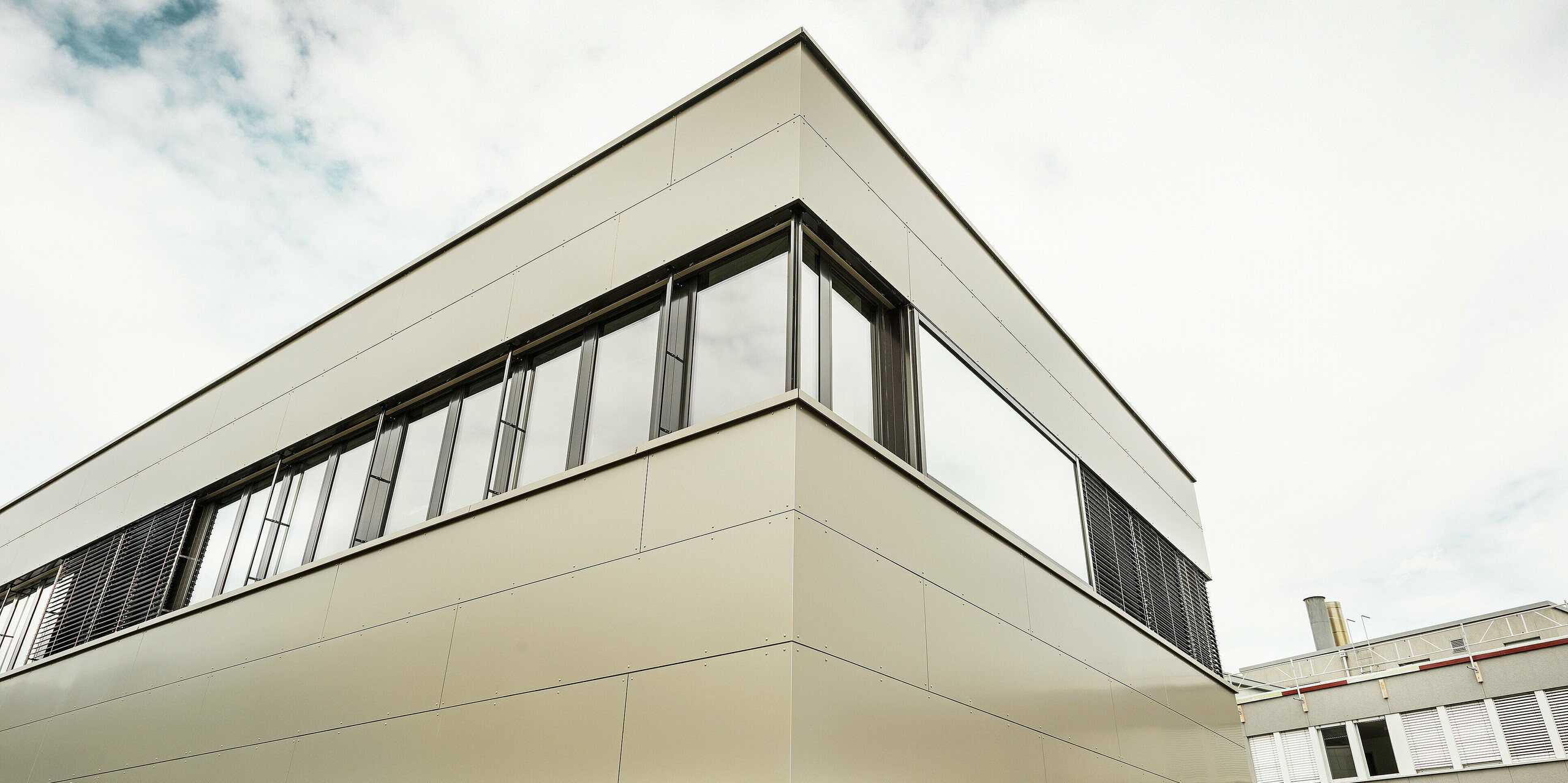 Die Nahaufnahme der Gebäudeecke zeigt die hochwertige PREFA Aluminiumfassade mit klar definierten Fugenbildern. Die edle Bronzefarbe der Aluminium Verbundplatten verleiht dem Firmengebäude eine exklusive, langlebige Außenwirkung.