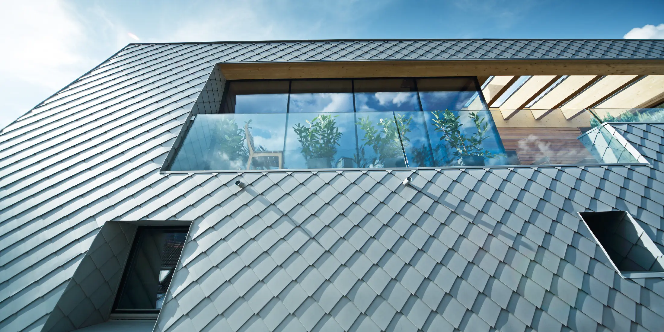 Modern ausgebautes Dachgeschoss mit großflächiger Dachterrasse, bodentiefen Glasfronten und patinagrauer Dachdeckung in Rautenoptik, die fließend in die Fassade übergeht und zeitgemäße Architektur betont.