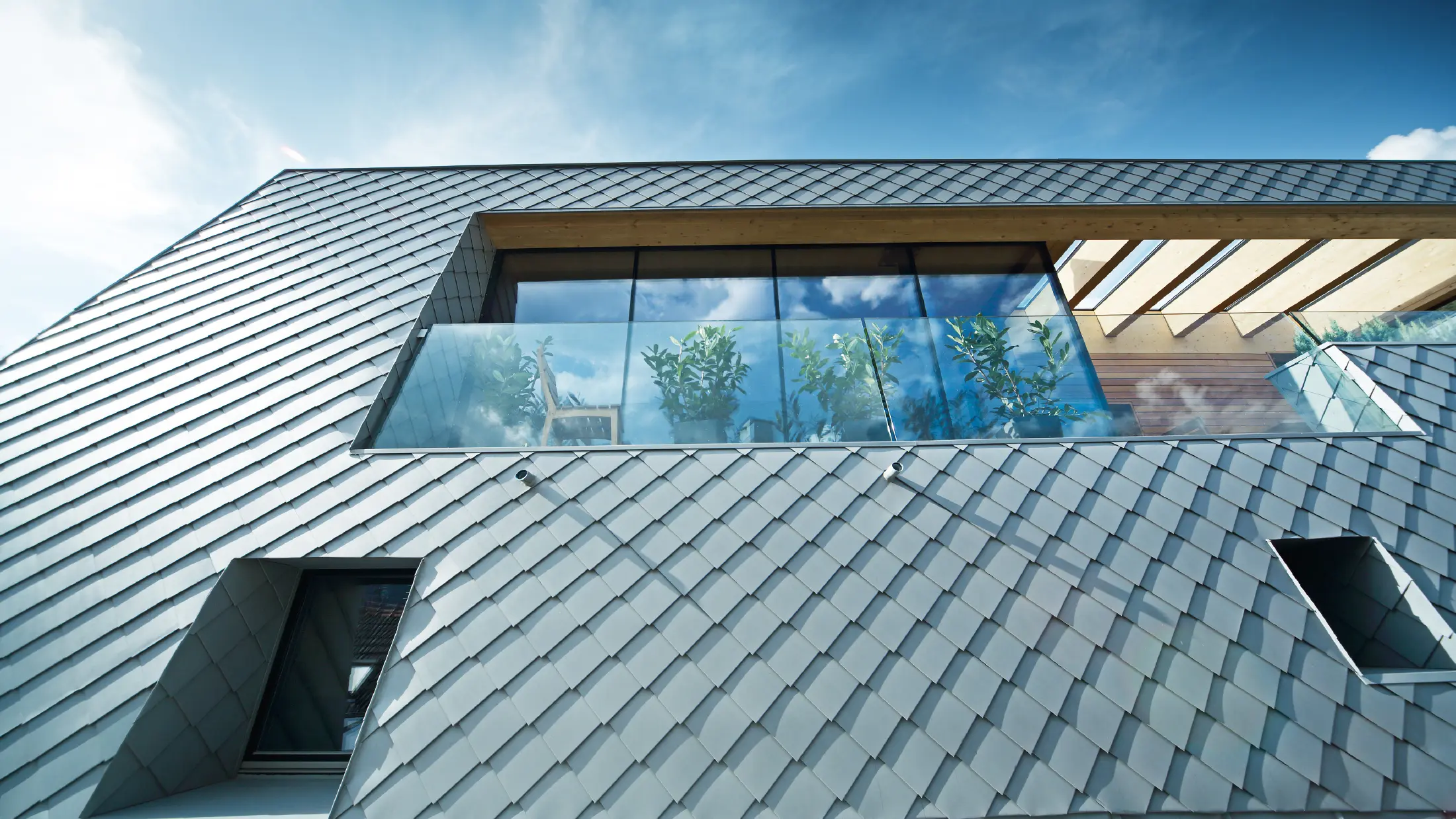 Modern ausgebautes Dachgeschoss mit großflächiger Dachterrasse, bodentiefen Glasfronten und patinagrauer Dachdeckung in Rautenoptik, die fließend in die Fassade übergeht und zeitgemäße Architektur betont.