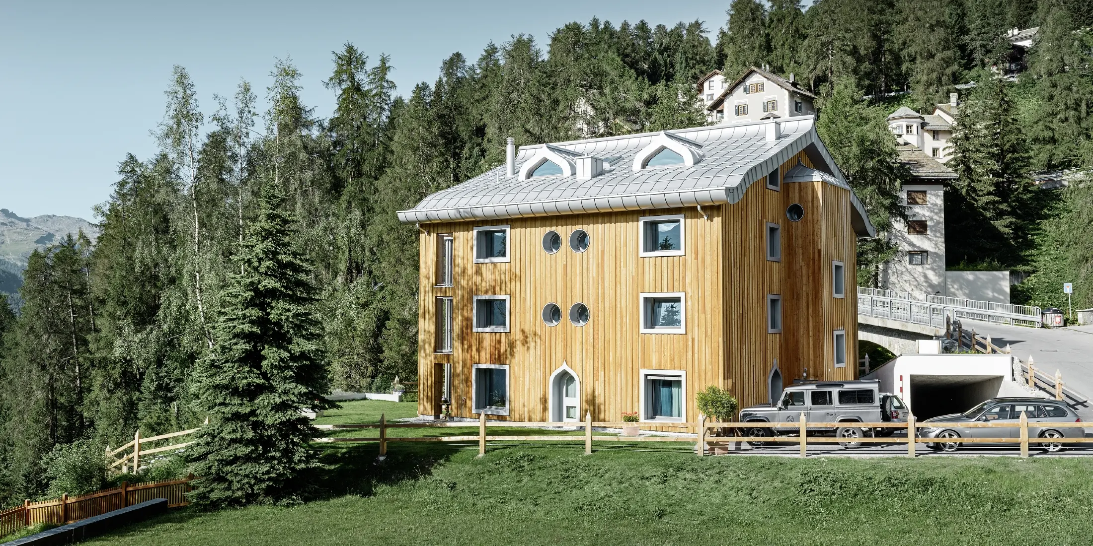 Wohnhausanlage in St. Moritz mit Holzfassade und Aluminiumdach mit geschwungener Traufe in silbermetallic