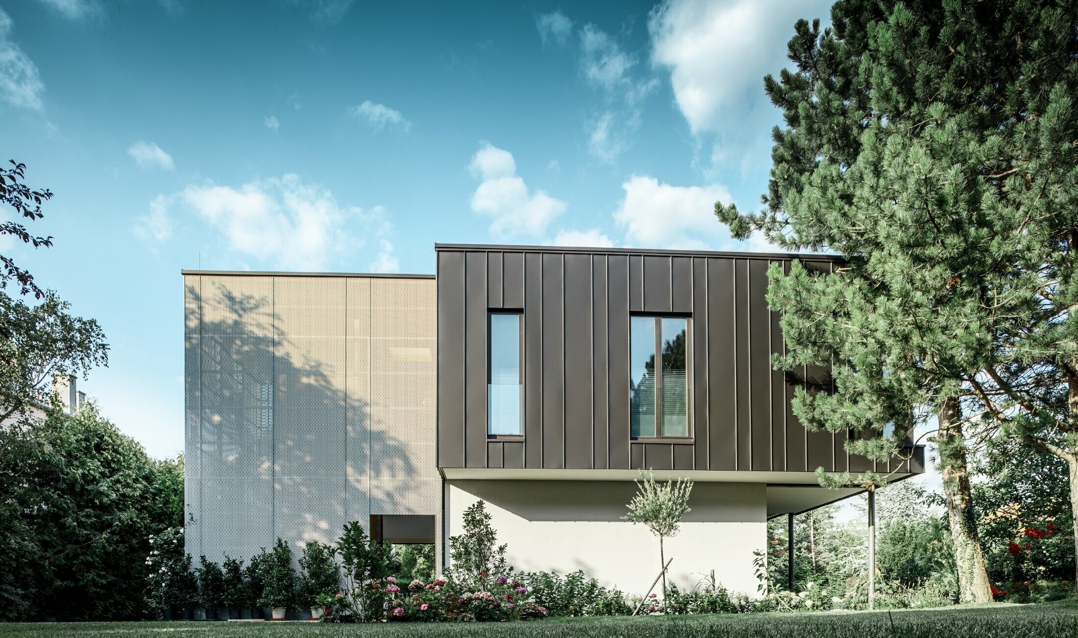 modernes Einfamilienhaus, ähnlich einem Baumhaus umgeben von einem großen Garten mit vielen Bäumen mit einer dezenten Winkelstehfalzfassade in schwarzgrau von PREFA