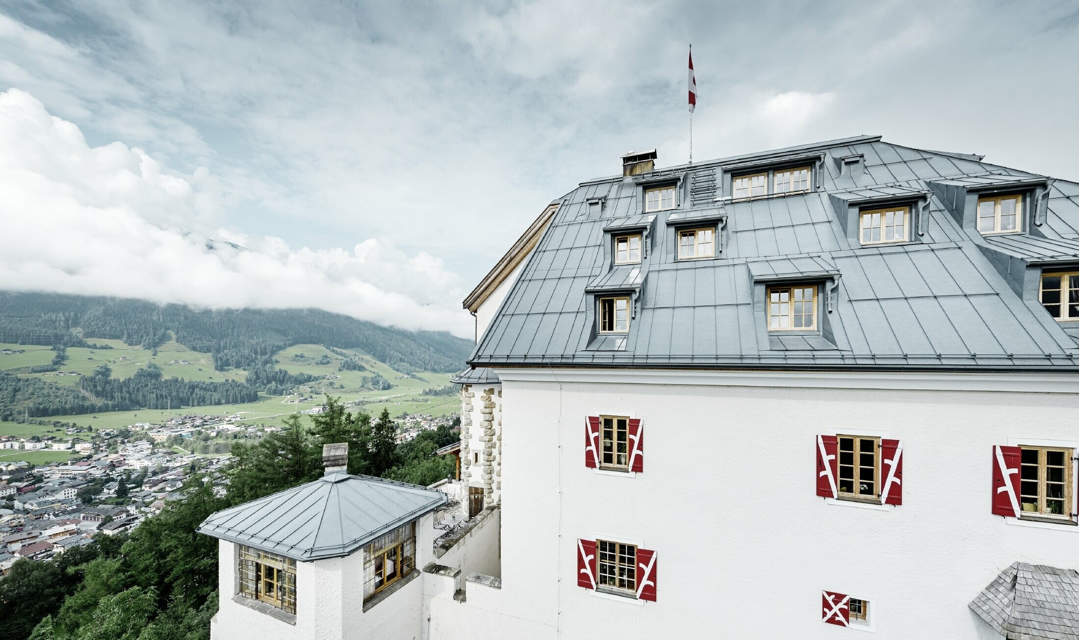 Schloss Mittersill umgeben von Bäumen und Bergen mit einem neu sanierten Prefalz Dach in steingrau