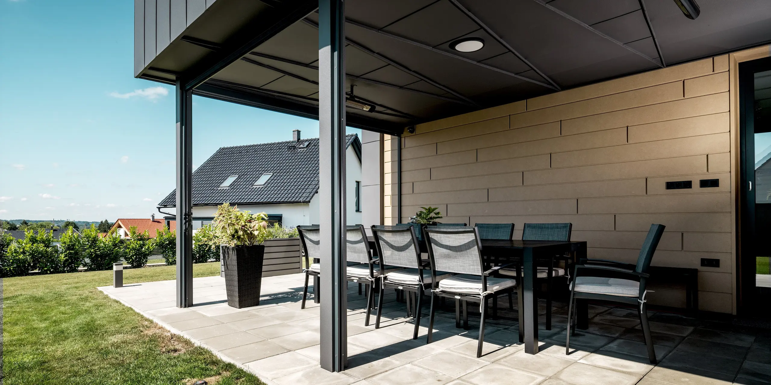 Die überdachte Terrasse verfügt über eine moderne PREFA Aluminiumfassade in der Farbe P.10 Sandbraun. Die langlebigen PREFA Sidings schaffen eine elegante Optik und vereinen Schutz, Beständigkeit und eine harmonische Gestaltung des Außenbereichs. Auch die Untersicht der Terrasse ist mit robustem Aluminium in einer außergewöhnlichen Falzmusterung verkleidet.