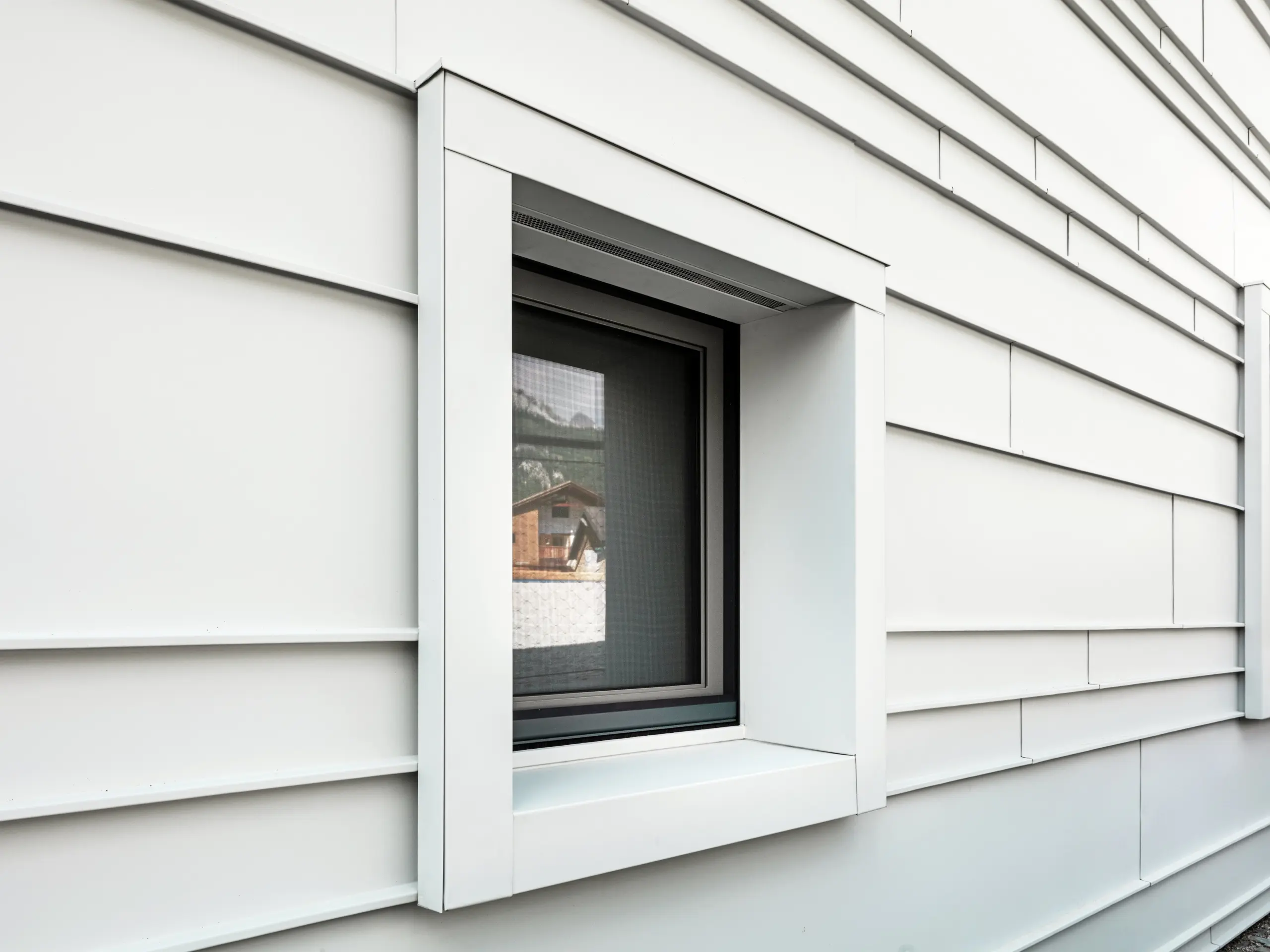 Detailansicht des markanten Fensterausschnitts in der hinterlüfteten Fassade aus PREFALZ P.10 in der Farbe Prefaweiß. Horizontal angeordnete Aluminiumstreifen sorgen für Struktur, Klarheit und eine moderne Ästhetik. Die ausgeprägten Fensterrahmen der „Tempesti“-Kaserne beginnen und enden stets exakt an der Überlappungslinie. Dadurch wird die Aluminiumkonstruktion bewusst hervorgehoben.