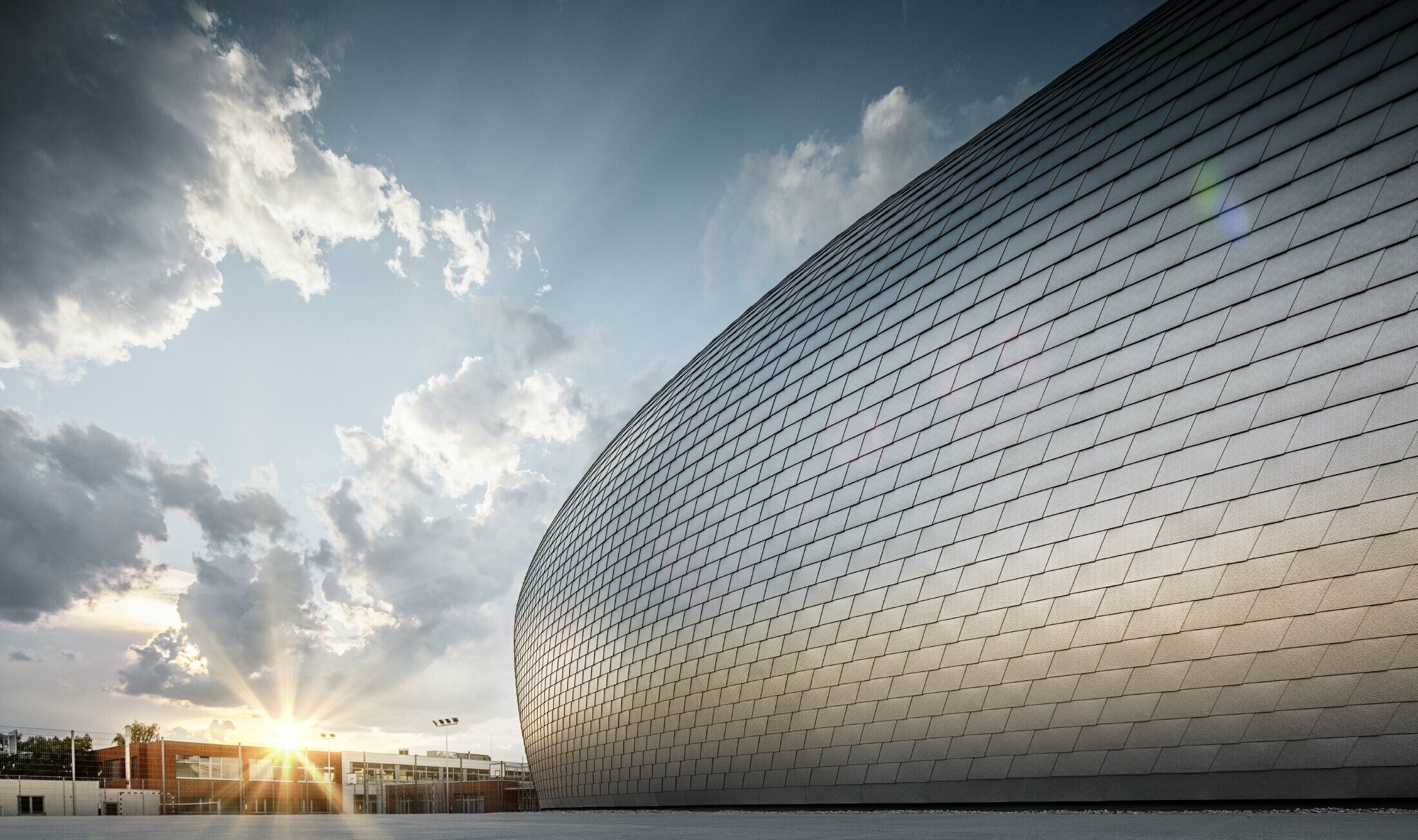 Sporthalle in Tschechien in Form eines UFOs verkleidet mit der PREFA Wandschindel in Naturblank bei Sonnenaufgang.