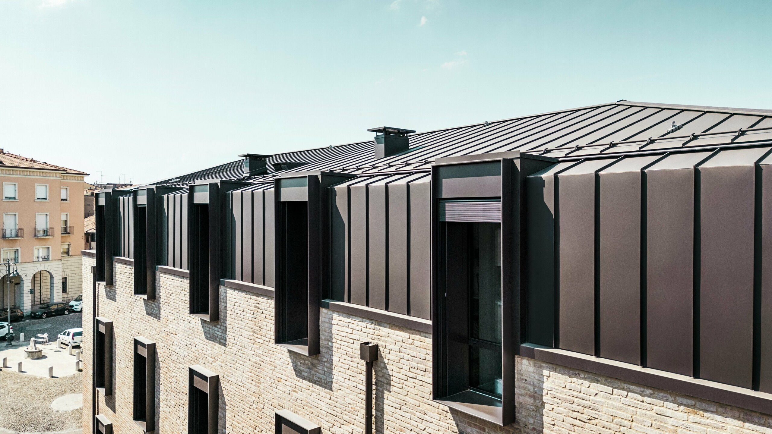 Moderan dizajn krova i fasade kuće od opeke u Italiji s PREFALZ aluminijskim krovom u boji P.10 smeđa lješnjaka i upečatljivim krovnim prozorima (zabatima).