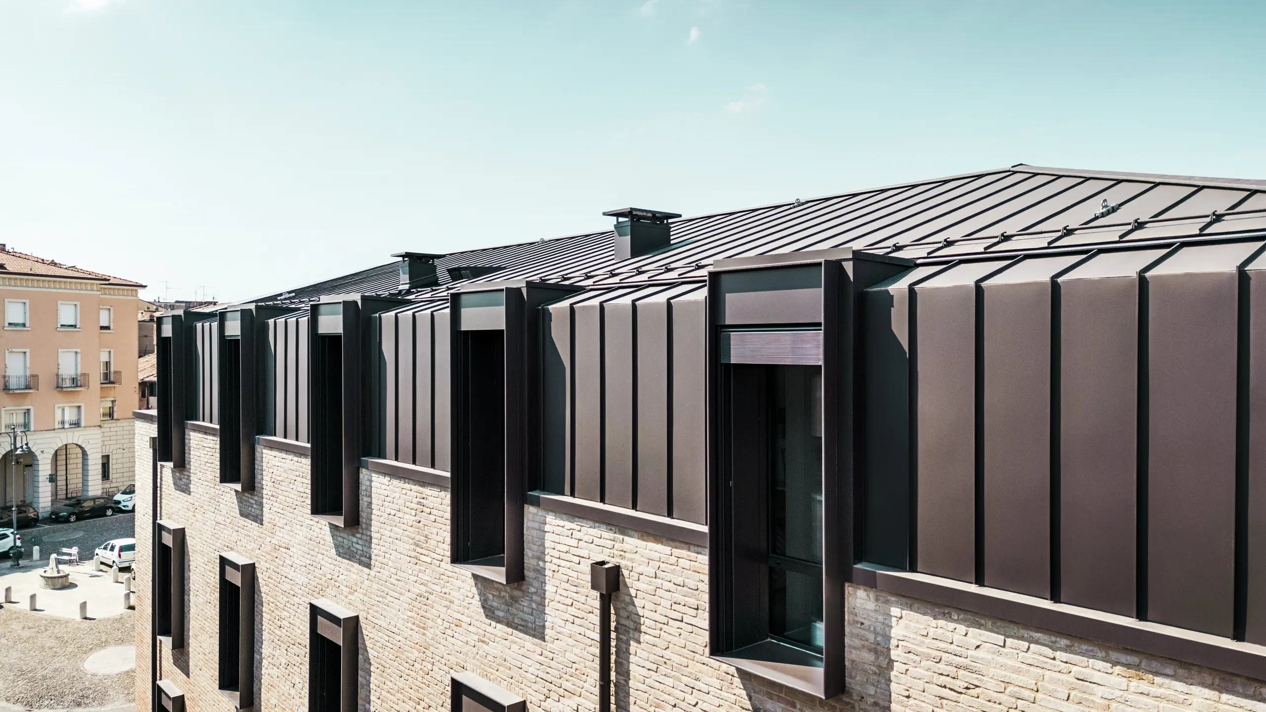 Modernes Dach- und Fassadendesign eines Backsteinhauses in Italien mit PREFALZ Aluminiumdach in P.10 Haselnussbraun und markanten Oberlichtern (Giebeln).